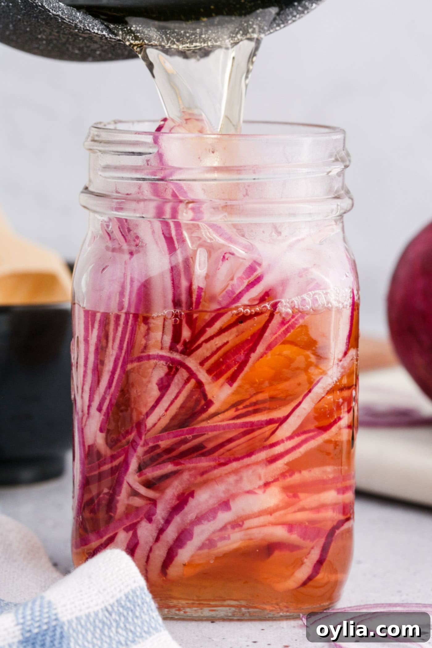 Pouring hot vinegar mixture over thinly sliced red onions in a mason jar