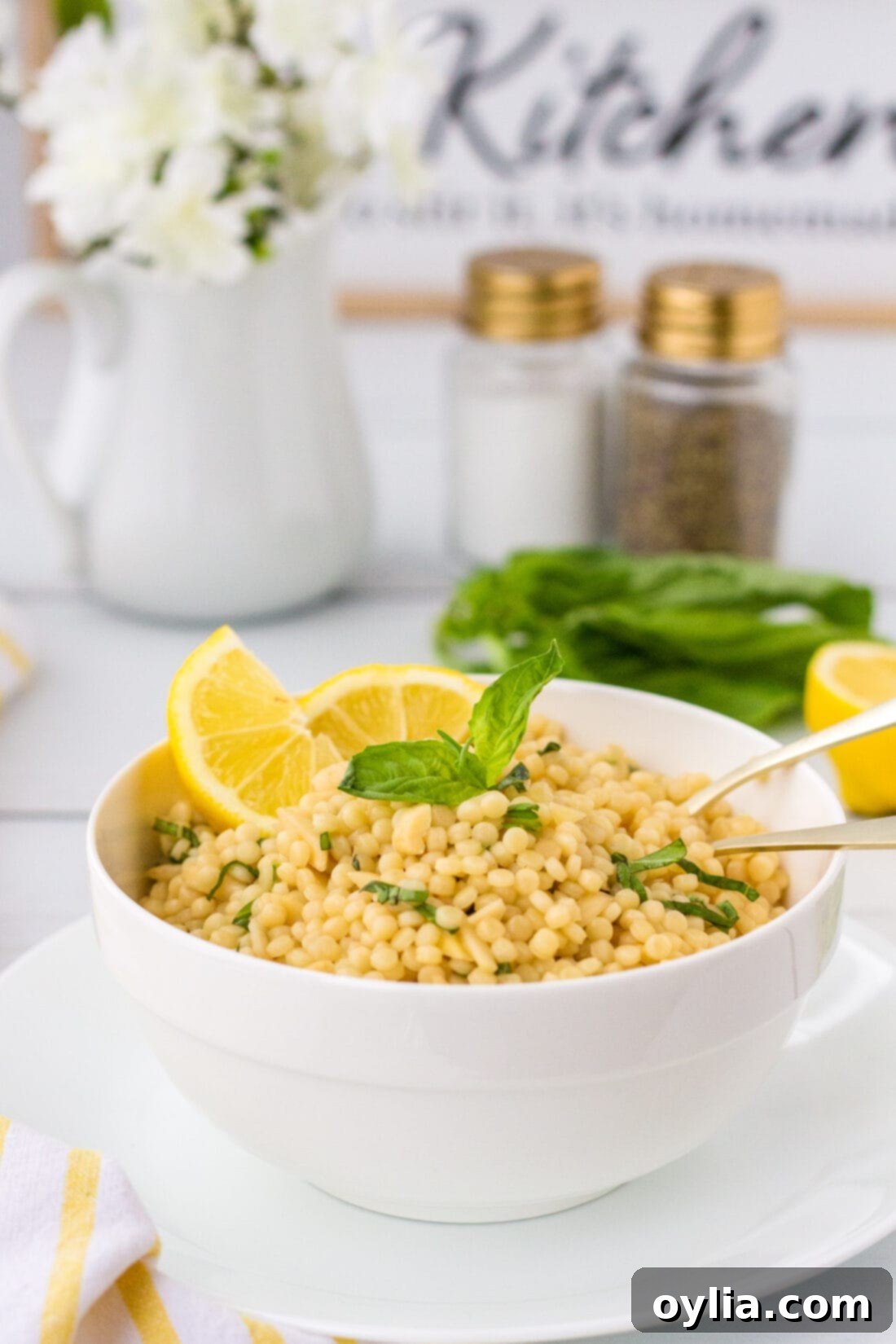 Sunshine Lemon Couscous 3 Lemon Couscous in a white bowl, with a salt shaker and pepper mill out of focus in the background, suggesting a fresh, seasoned dish.