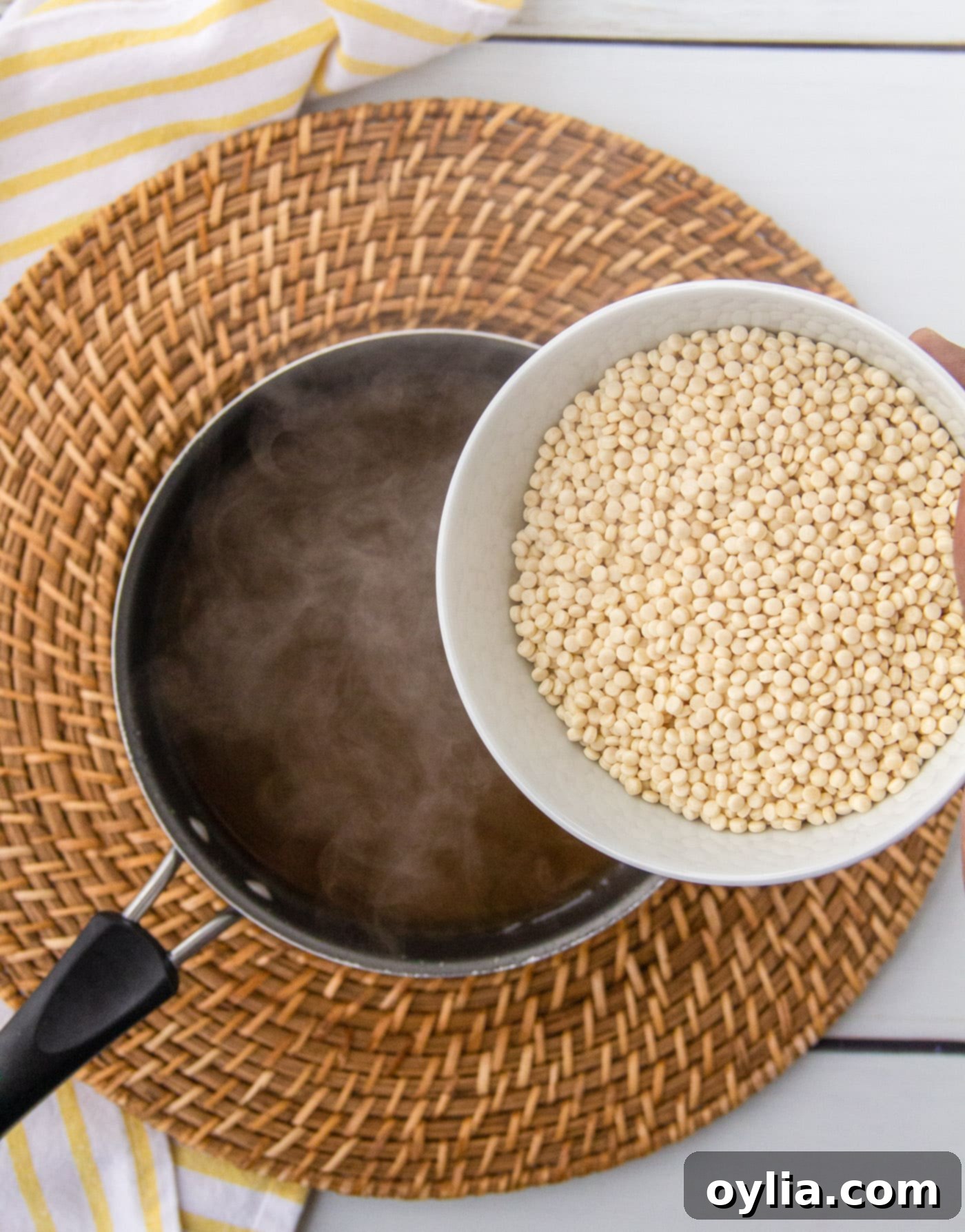 Pearl couscous being poured into a saucepan of simmering broth, illustrating the cooking process for the lemon couscous.