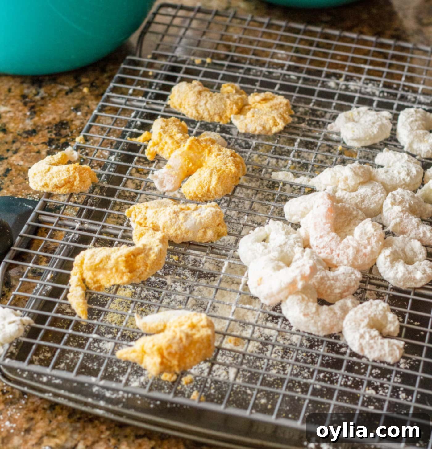 Breaded shrimp resting on a wire cooling rack before frying to ensure a crispy coating.