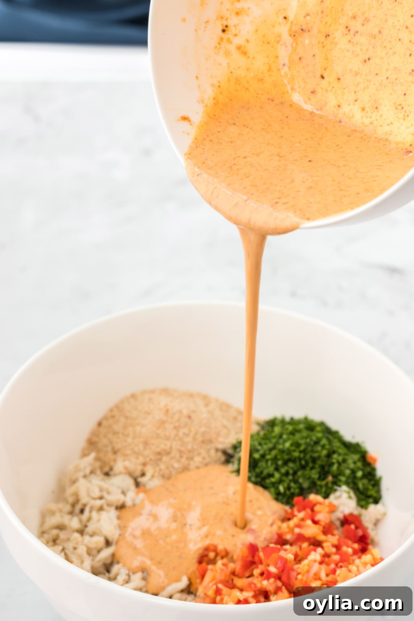 Pouring the seasoned mayonnaise mixture over crab cake ingredients in a bowl