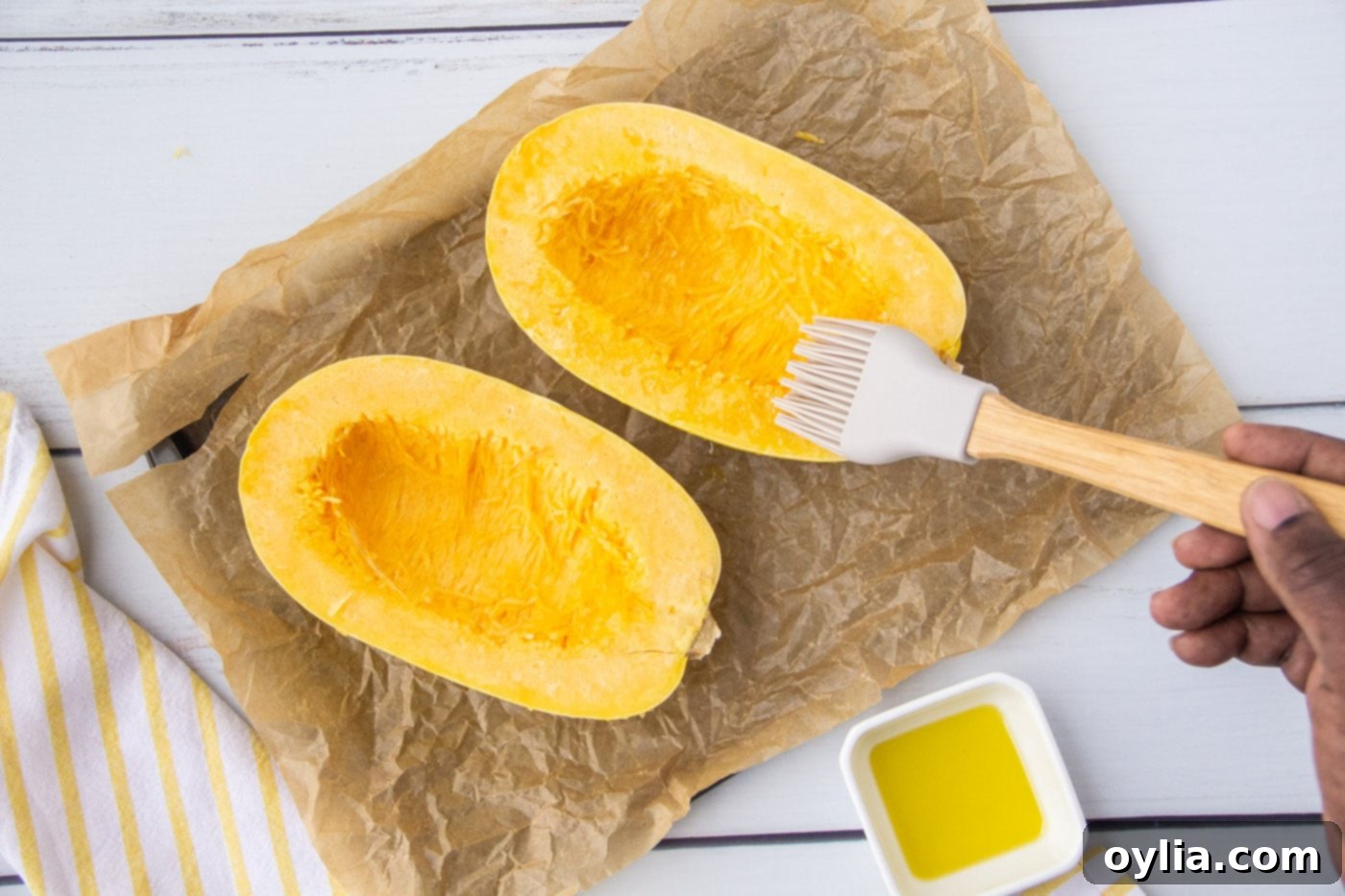 Olive oil being brushed onto the exposed flesh of a spaghetti squash half.