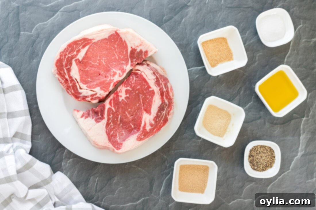 Collection of fresh ingredients for Reverse Sear Ribeye on a wooden board, including spices and olive oil