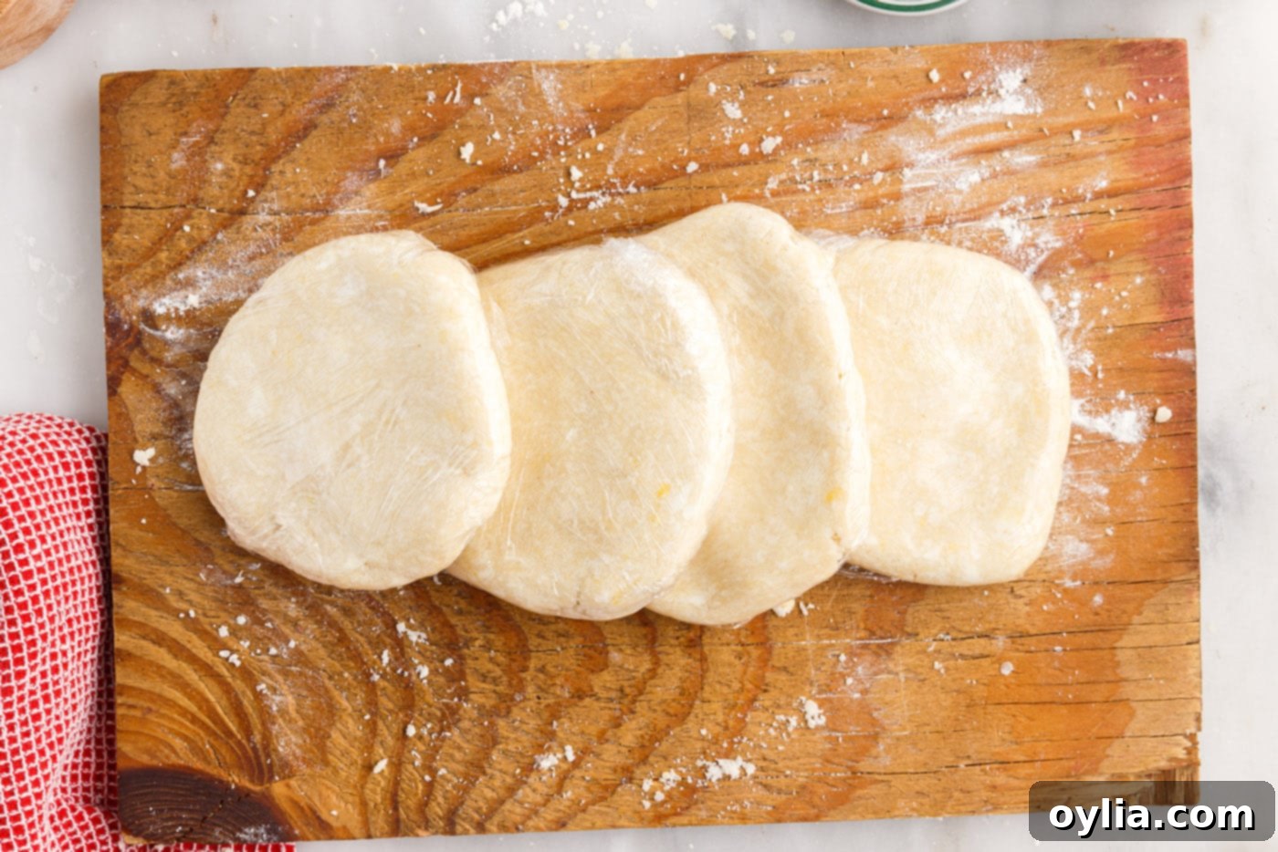 Four flattened discs of rugelach dough, each wrapped in plastic wrap, ready for chilling.