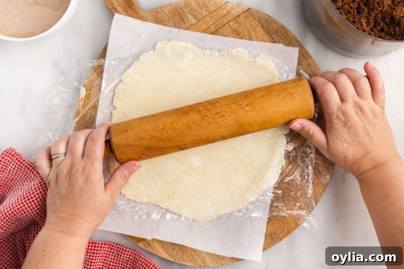A rolling pin flattening the rugelach dough into a perfect circle on parchment paper.