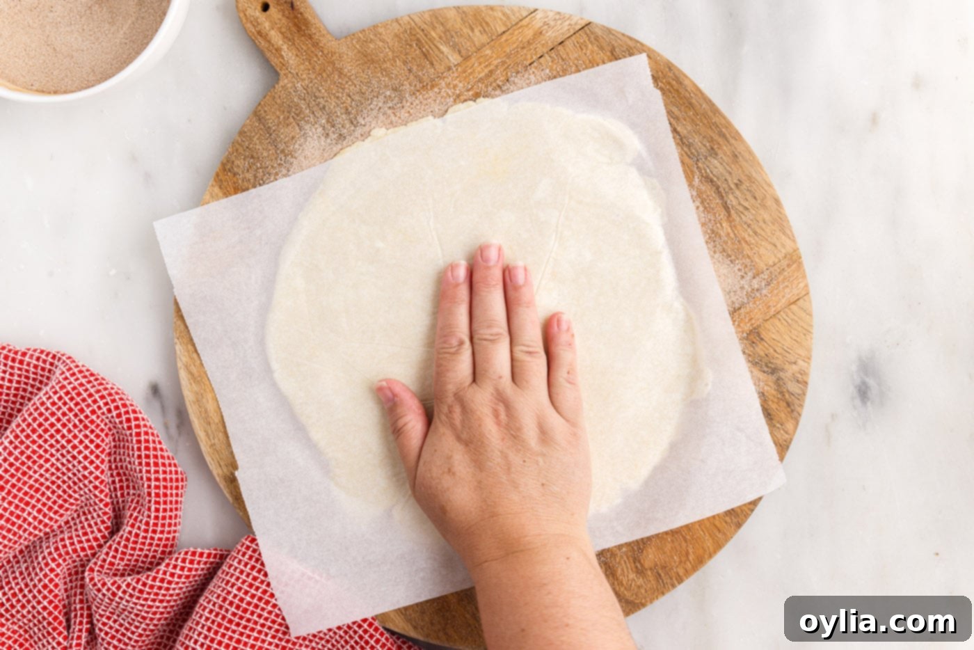 A hand gently pressing the rugelach dough disc onto the cinnamon sugar sprinkled on parchment paper, ensuring it sticks.