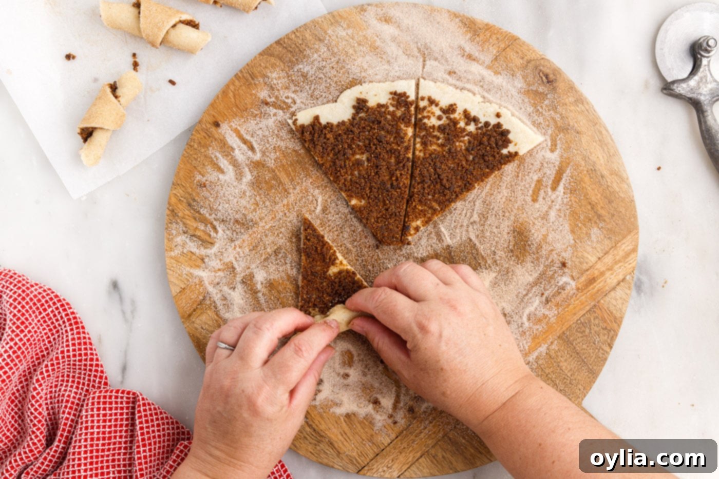 Hands carefully rolling a rugelach dough wedge from the wide end towards the center to form a crescent shape.