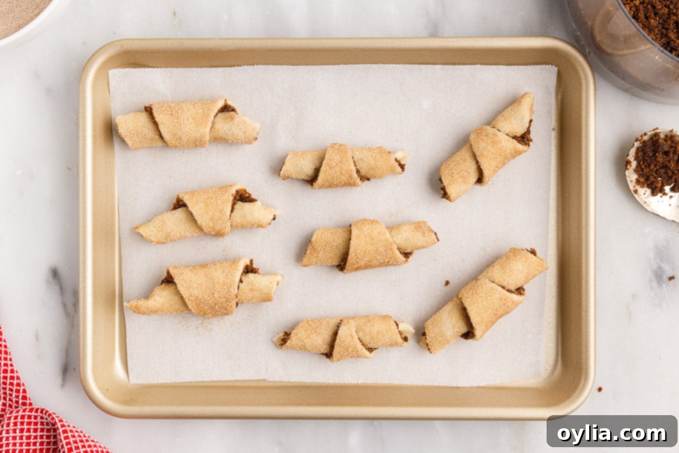 Unbaked rugelach crescent rolls arranged on a parchment-lined cutting board, ready for the oven.