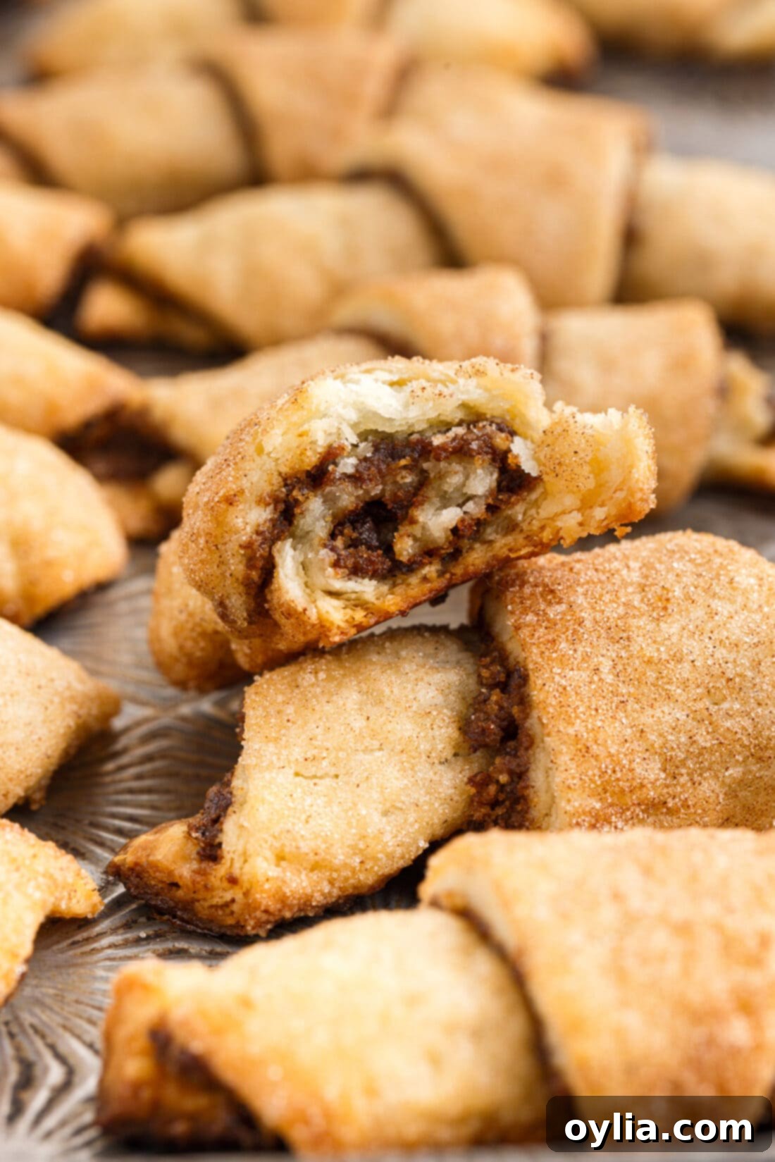 A single piece of Rugelach with a bite taken out, revealing the delicious layers of flaky dough and the sweet walnut, cinnamon, and raisin filling.
