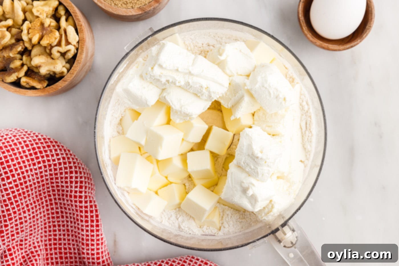 Cold cream cheese and butter cubes over flour in a food processor bowl, ready to be pulsed.