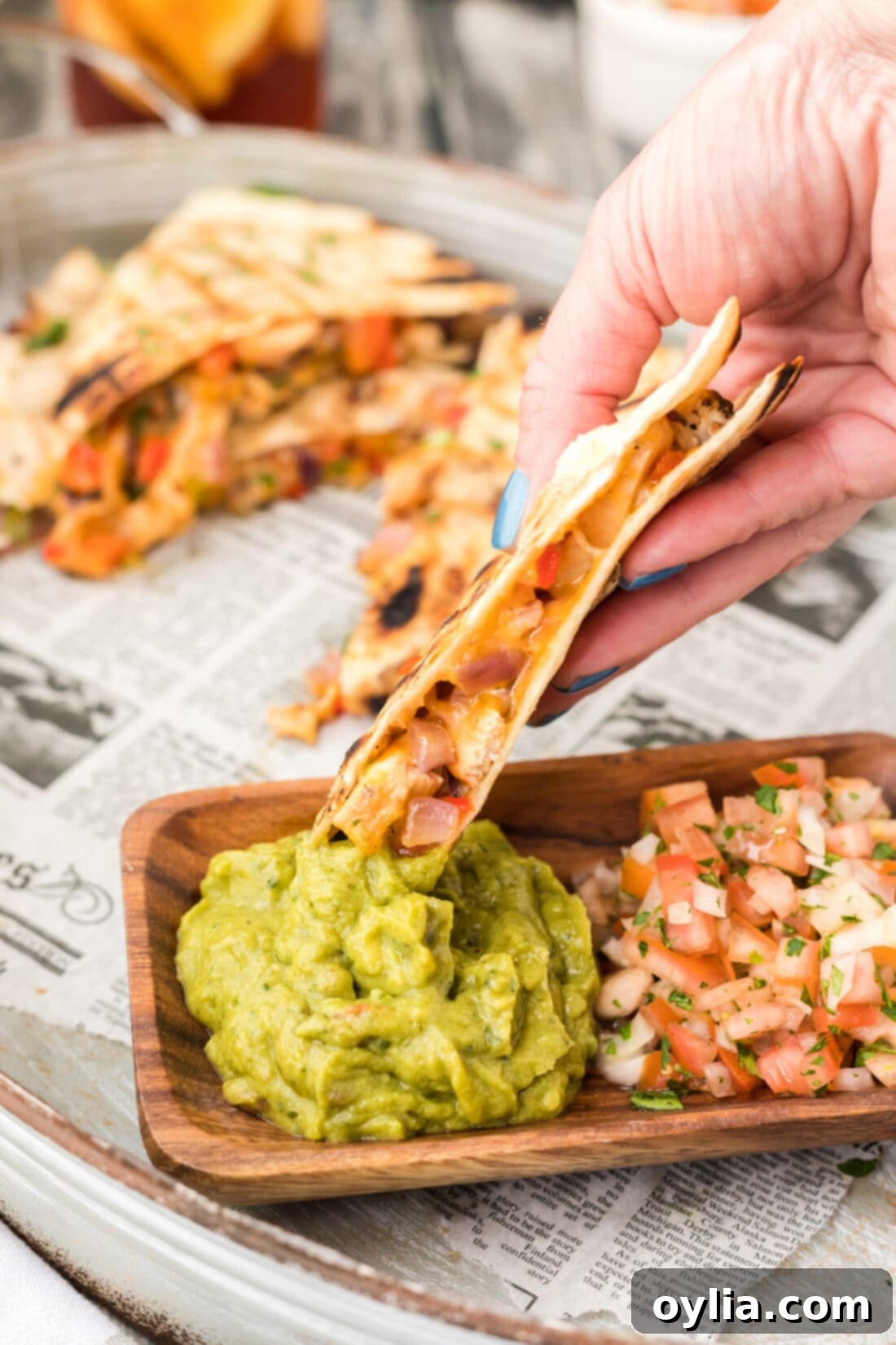 Ultimate Grilled Chicken Quesadilla 11 Hand dipping a freshly grilled chicken quesadilla triangle into a bowl of vibrant green guacamole