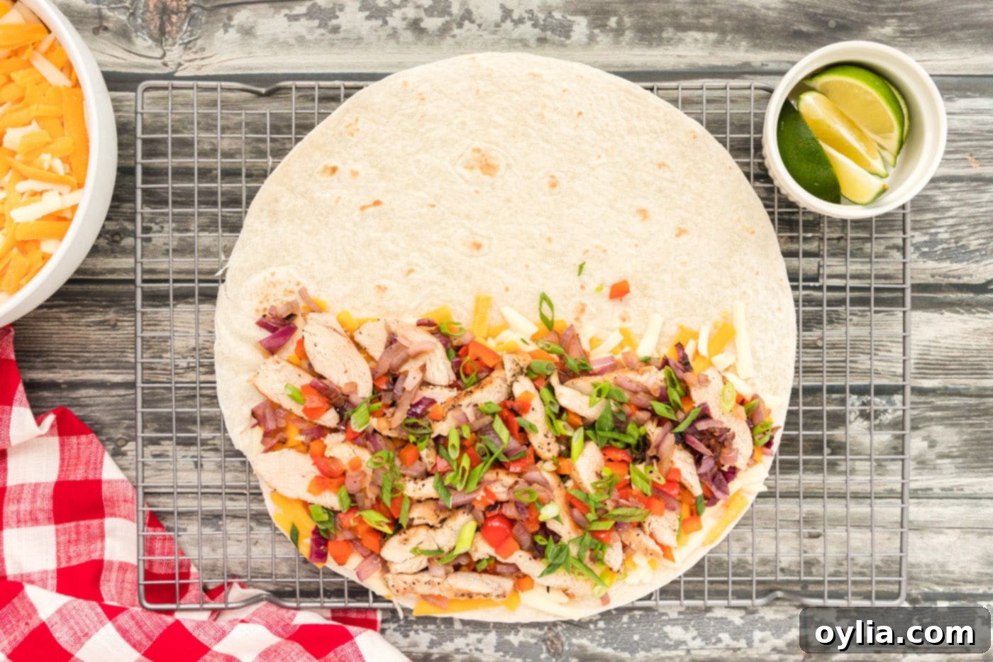 Sliced chicken, bell peppers, and onions spread over cheese on half of a tortilla