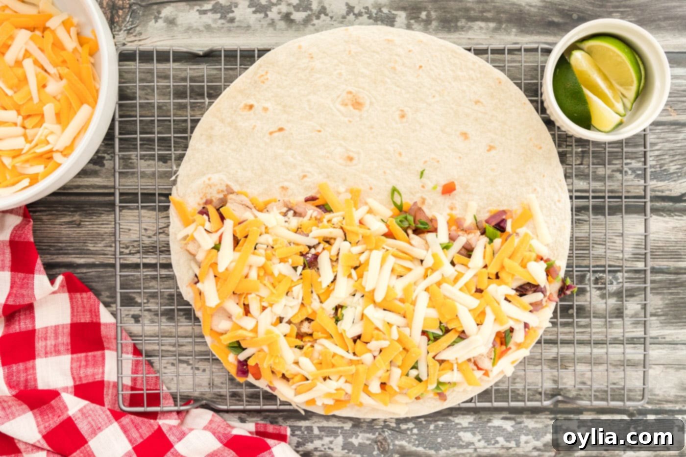 More shredded cheese covering chicken and vegetables on a tortilla