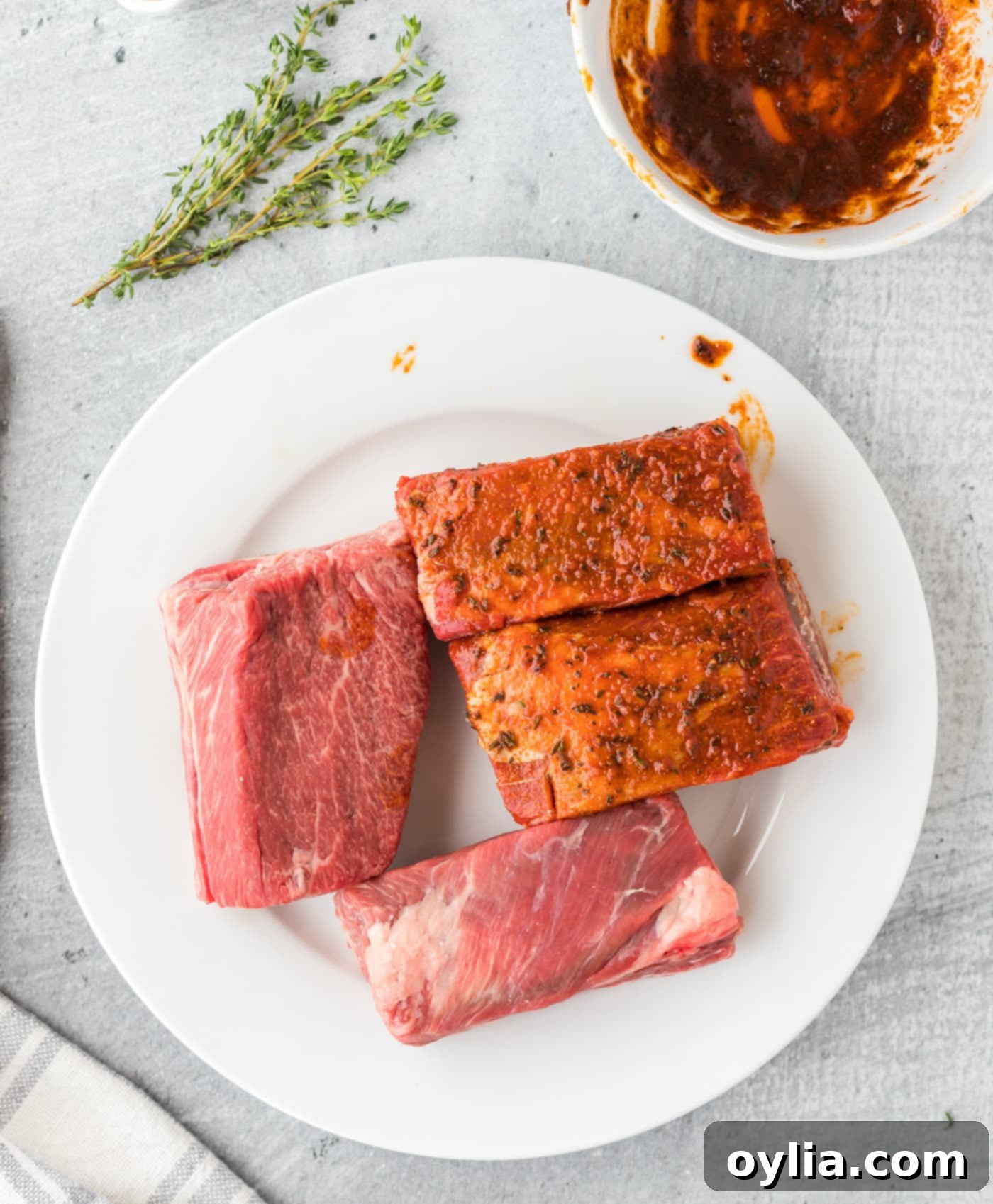 Hands rubbing seasoning into beef short ribs on a plate