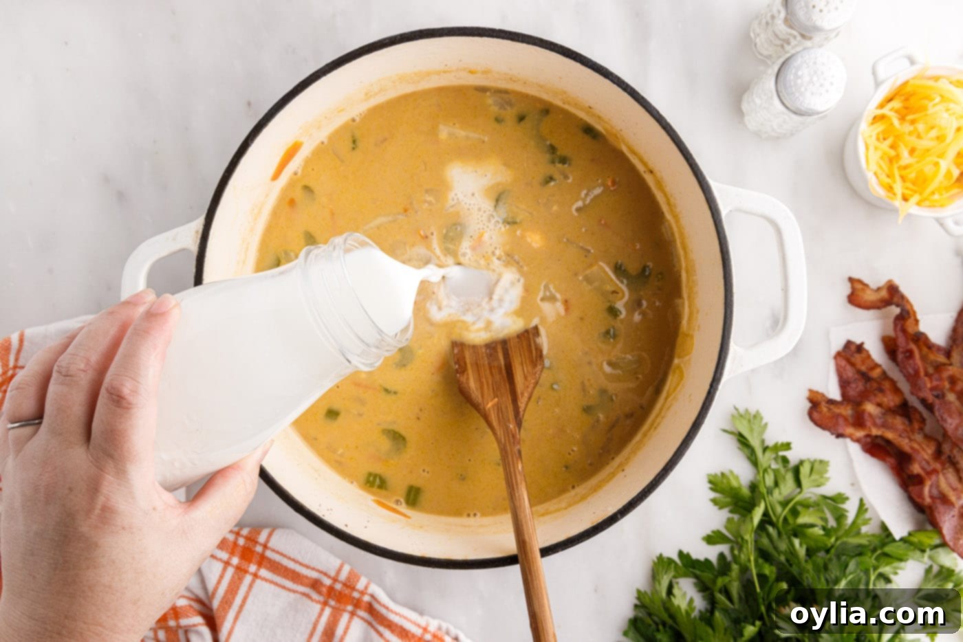 Pouring milk into the simmering cheeseburger soup with cheese and beef, stirring to combine