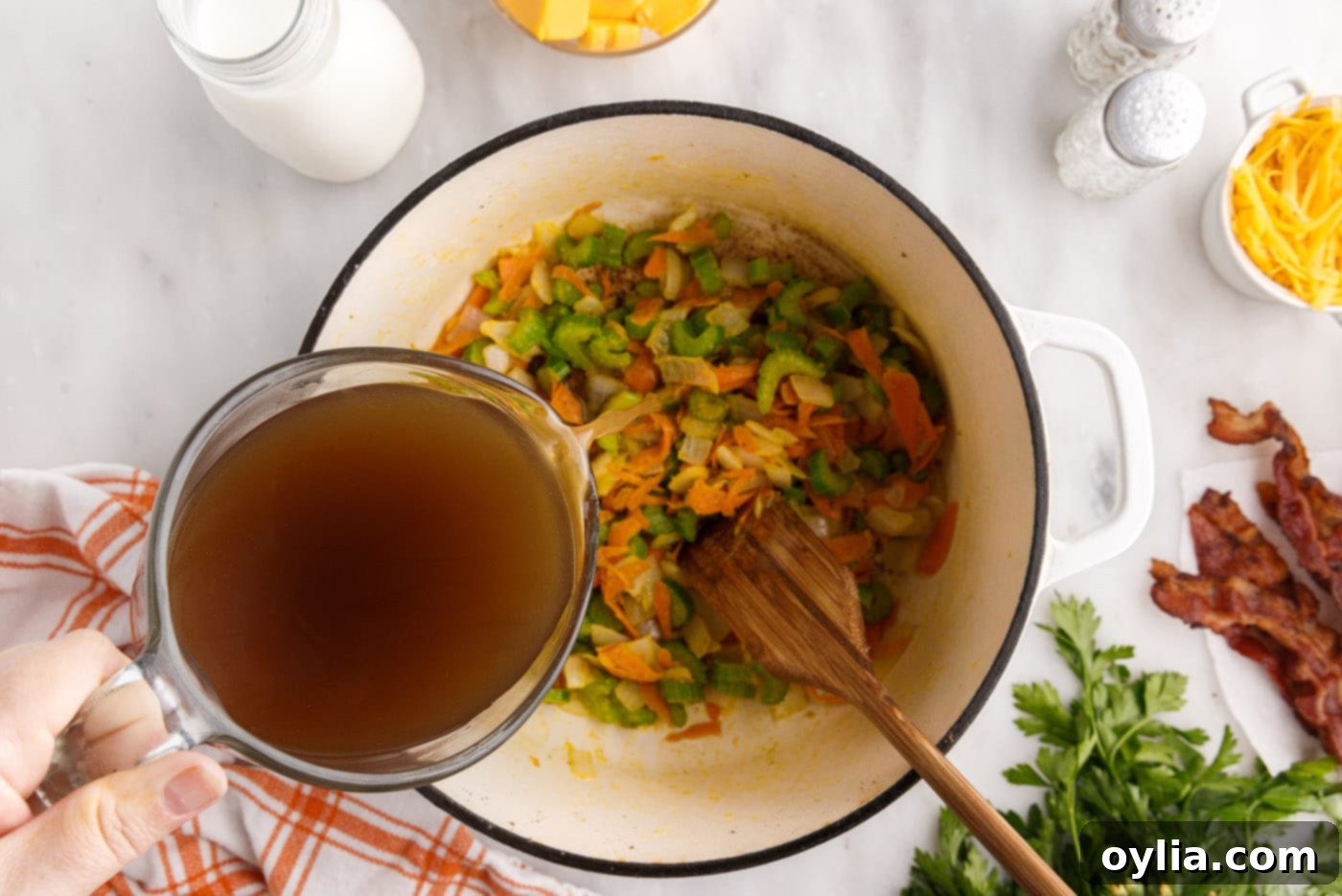 Pouring beef broth into the stockpot with vegetables and flour, stirring to combine
