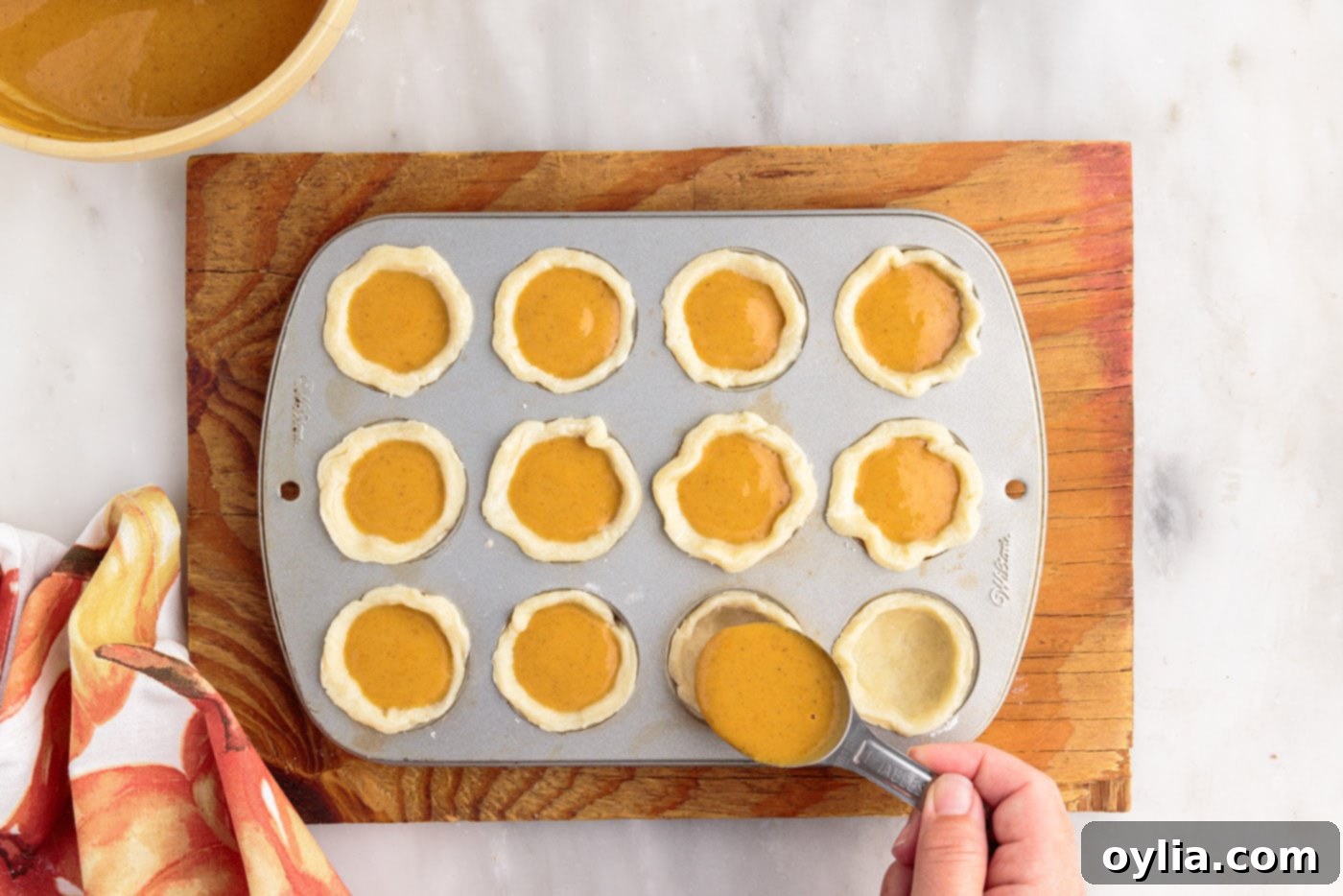 Adding pumpkin pie filling to mini pie crusts in a muffin pan