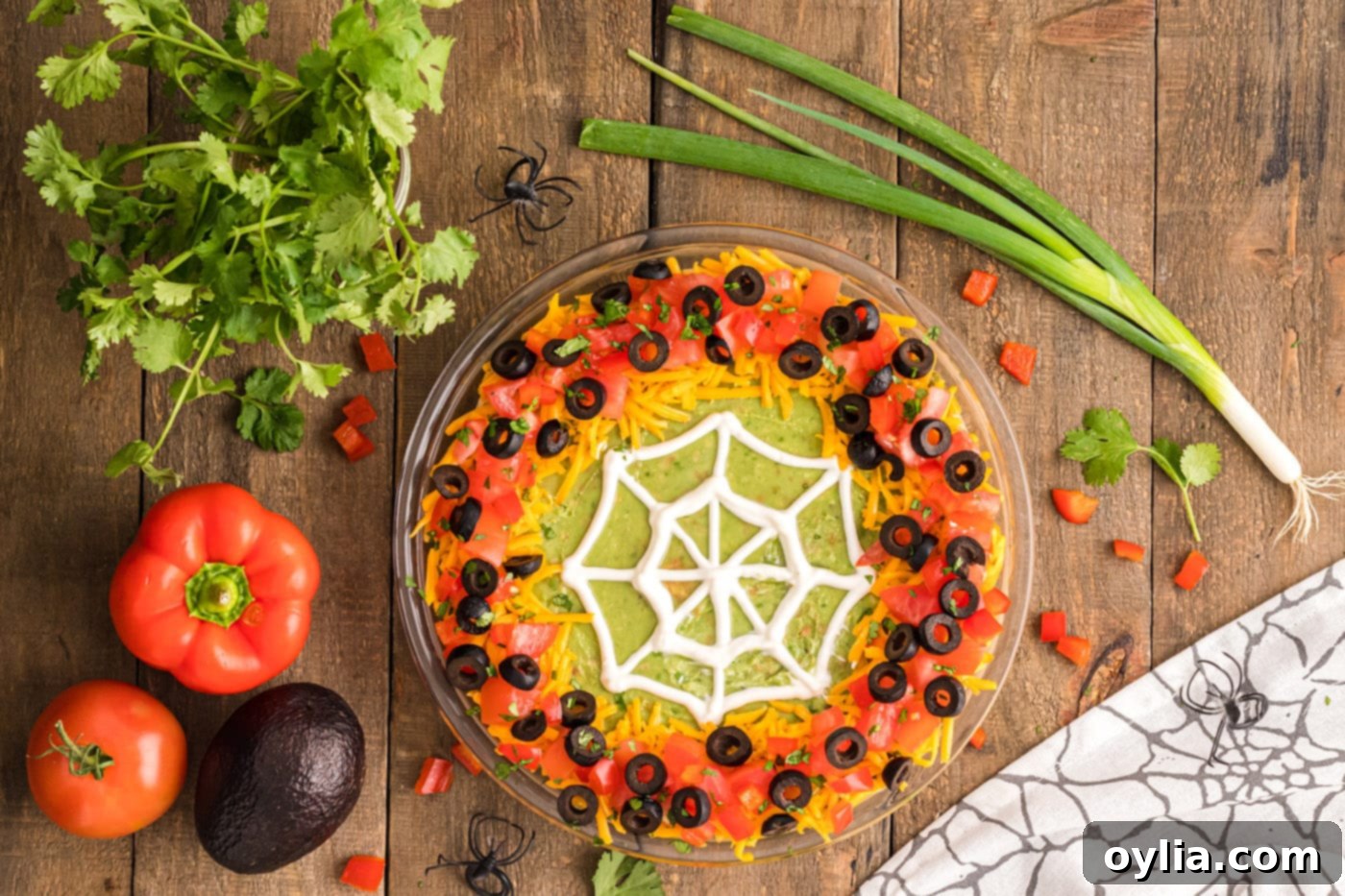 overhead view of Spider Web Taco Dip with all toppings, including tomatoes, olives, and cilantro, surrounding the web