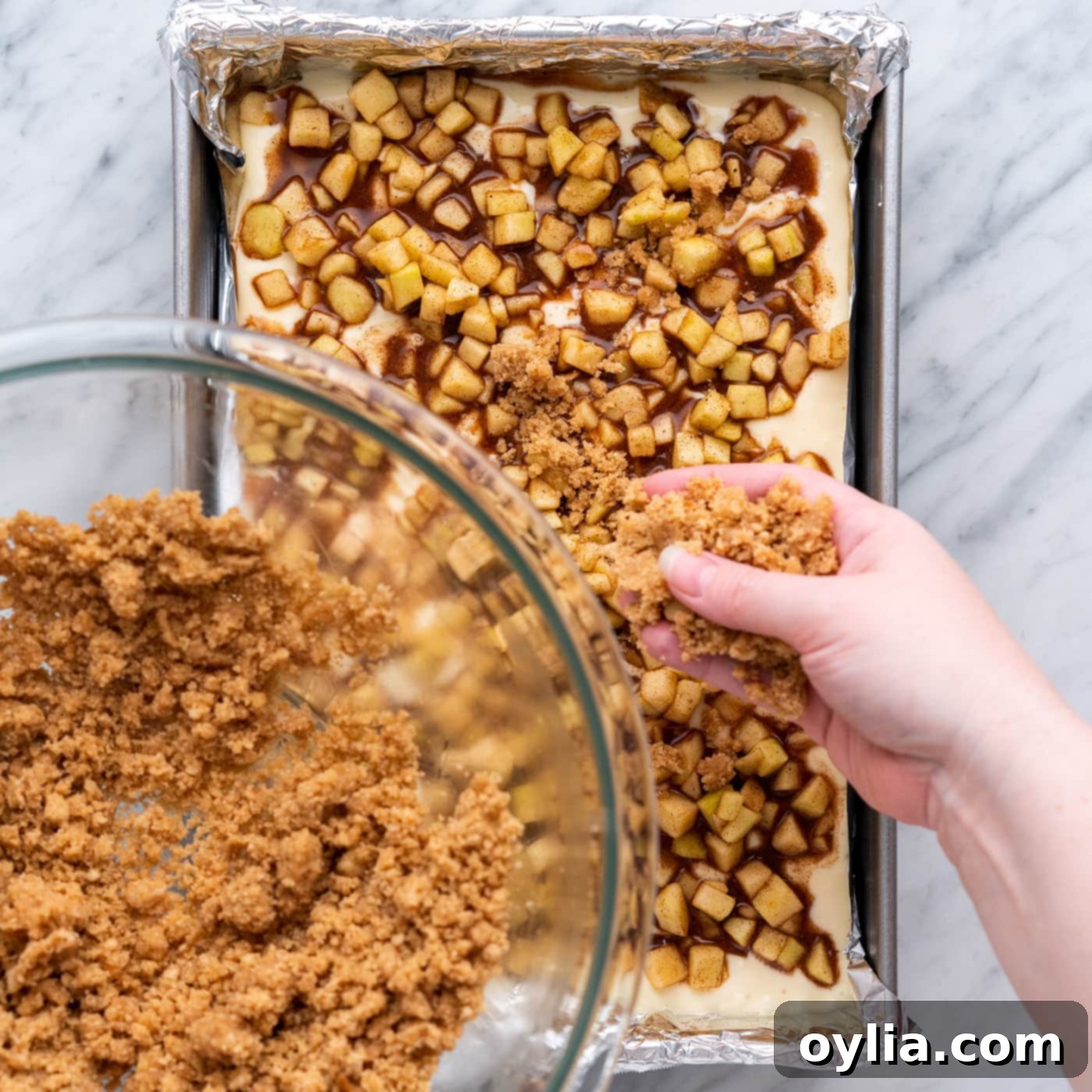 sprinkling streusel topping on top of caramel apple cheesecake bars