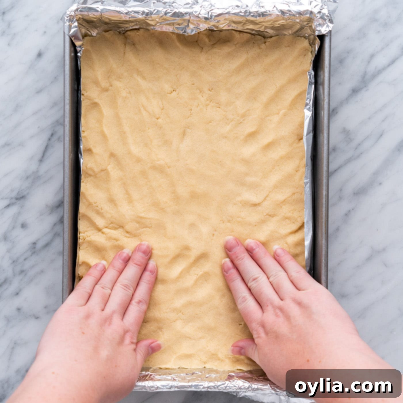 hands flattening shortbread crust in a baking pan