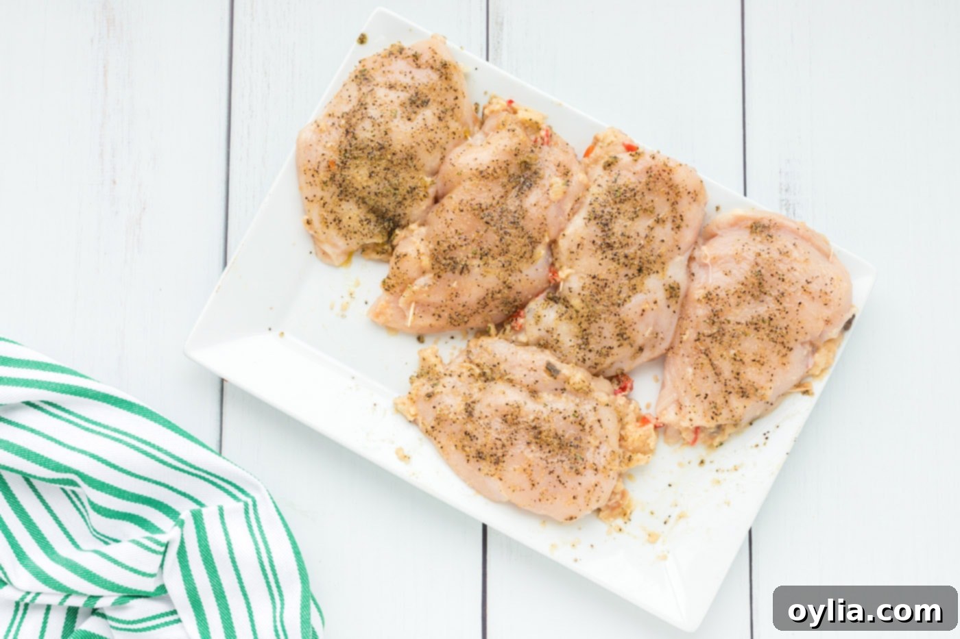 Seasoned stuffed chicken breasts on a cutting board, coated with olive oil, garlic salt, and pepper