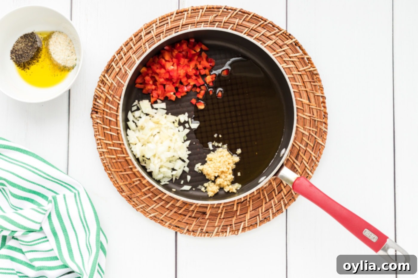 Red bell pepper, garlic, and onion gently sautéing in a skillet with olive oil