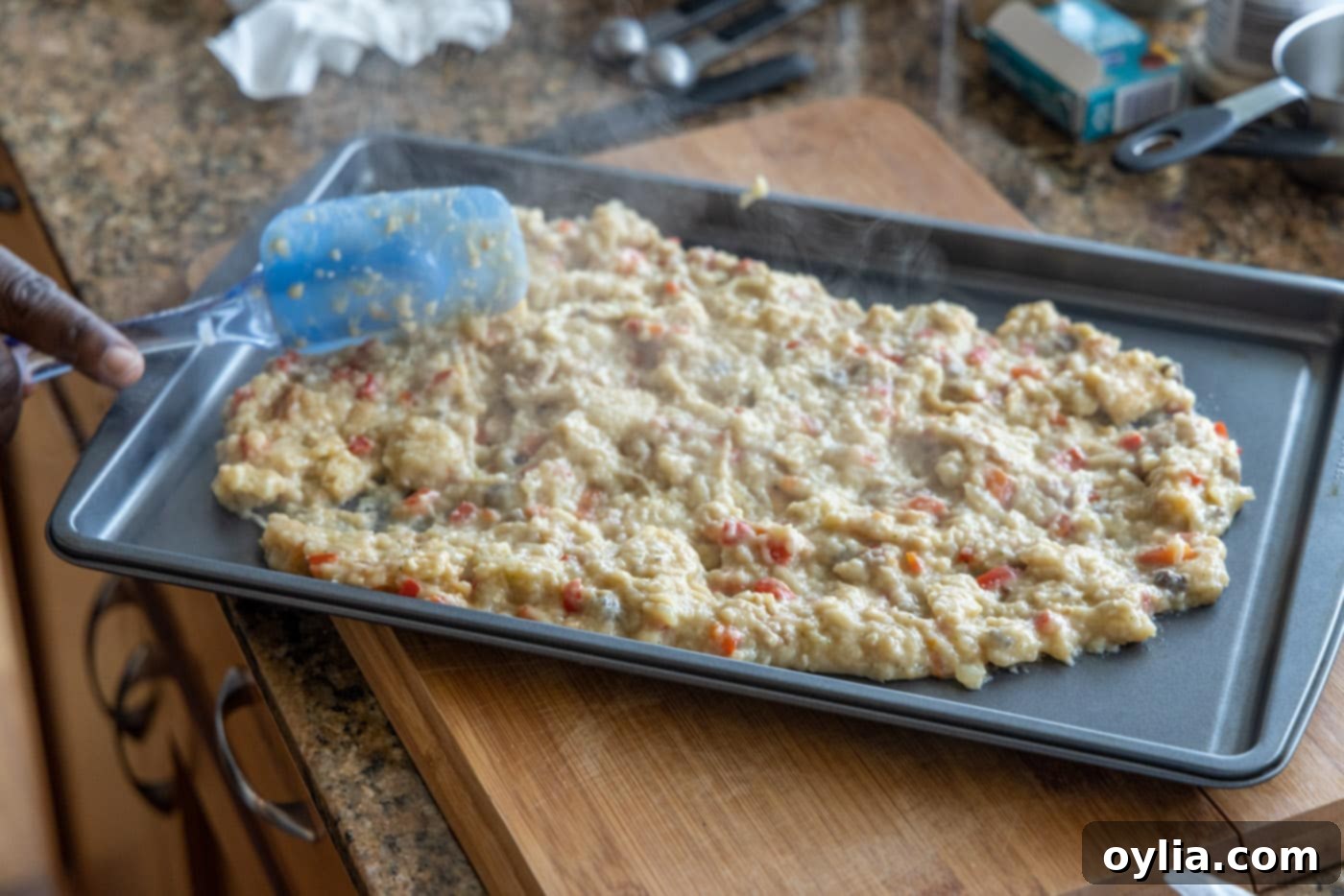 Spreading the warm stuffing mixture evenly onto a baking sheet to cool, preparing it for the chicken breasts