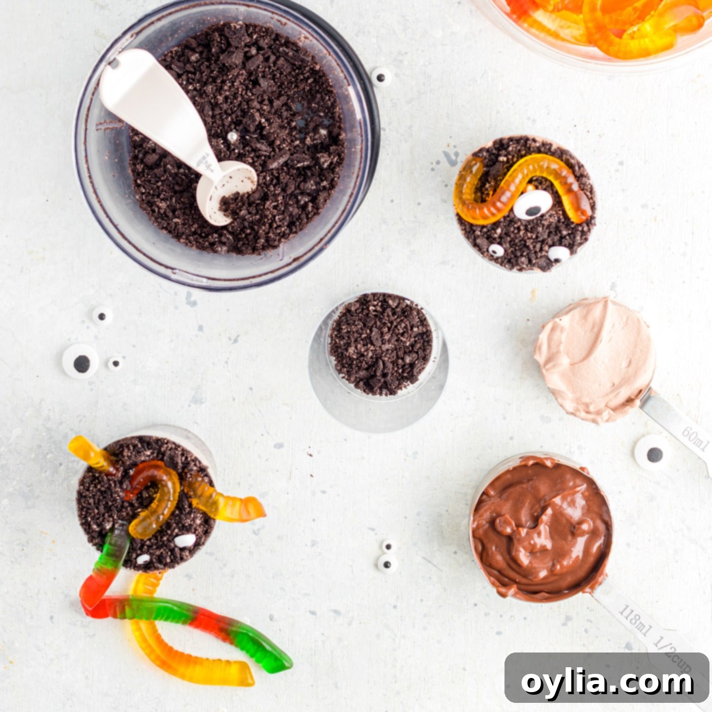 A kitchen counter set up for assembling Halloween Dirt Cups, with pudding, crushed Oreos, and empty plastic cups.