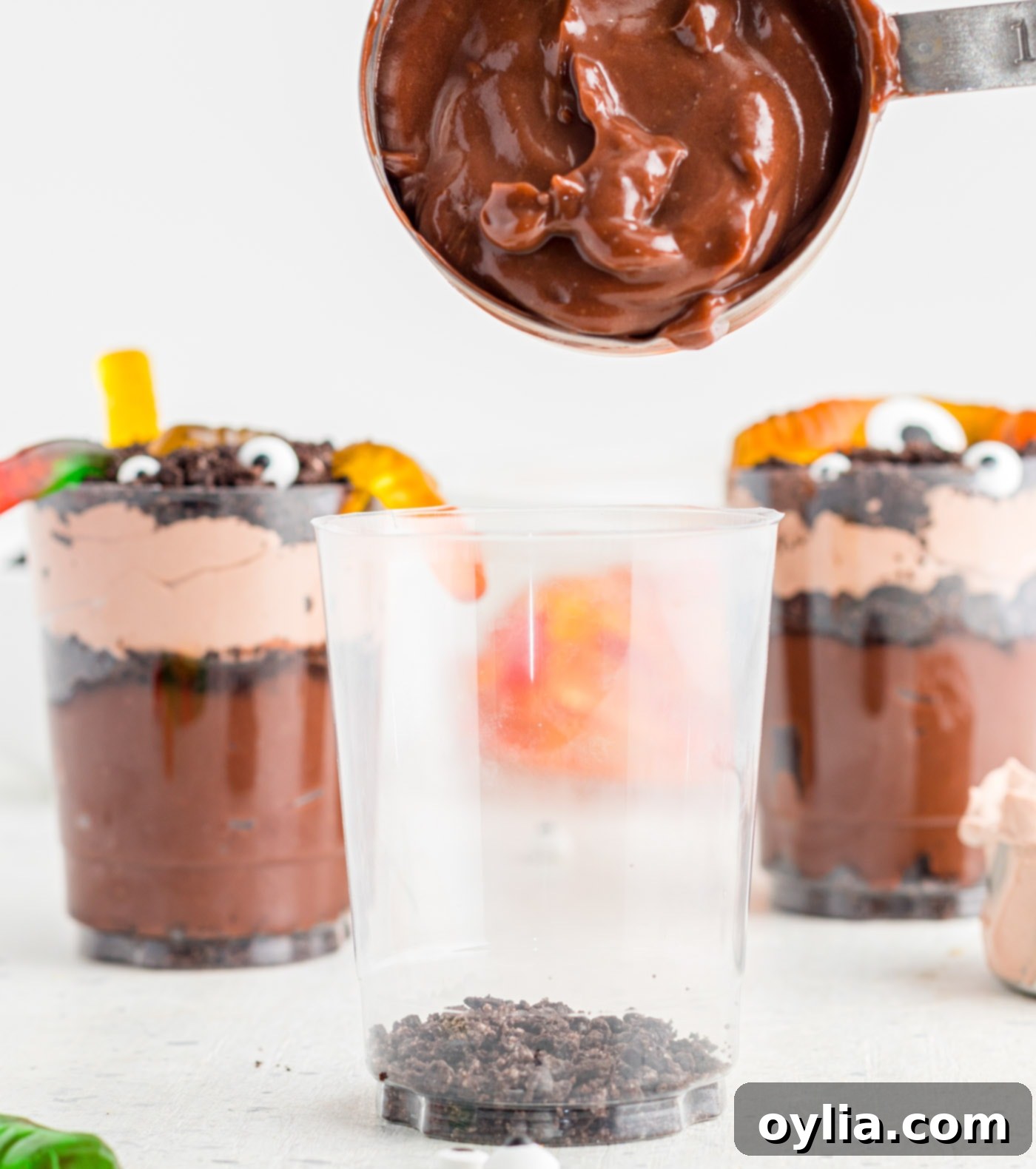 A spoon adding chocolate pudding as a layer in a clear dessert cup.