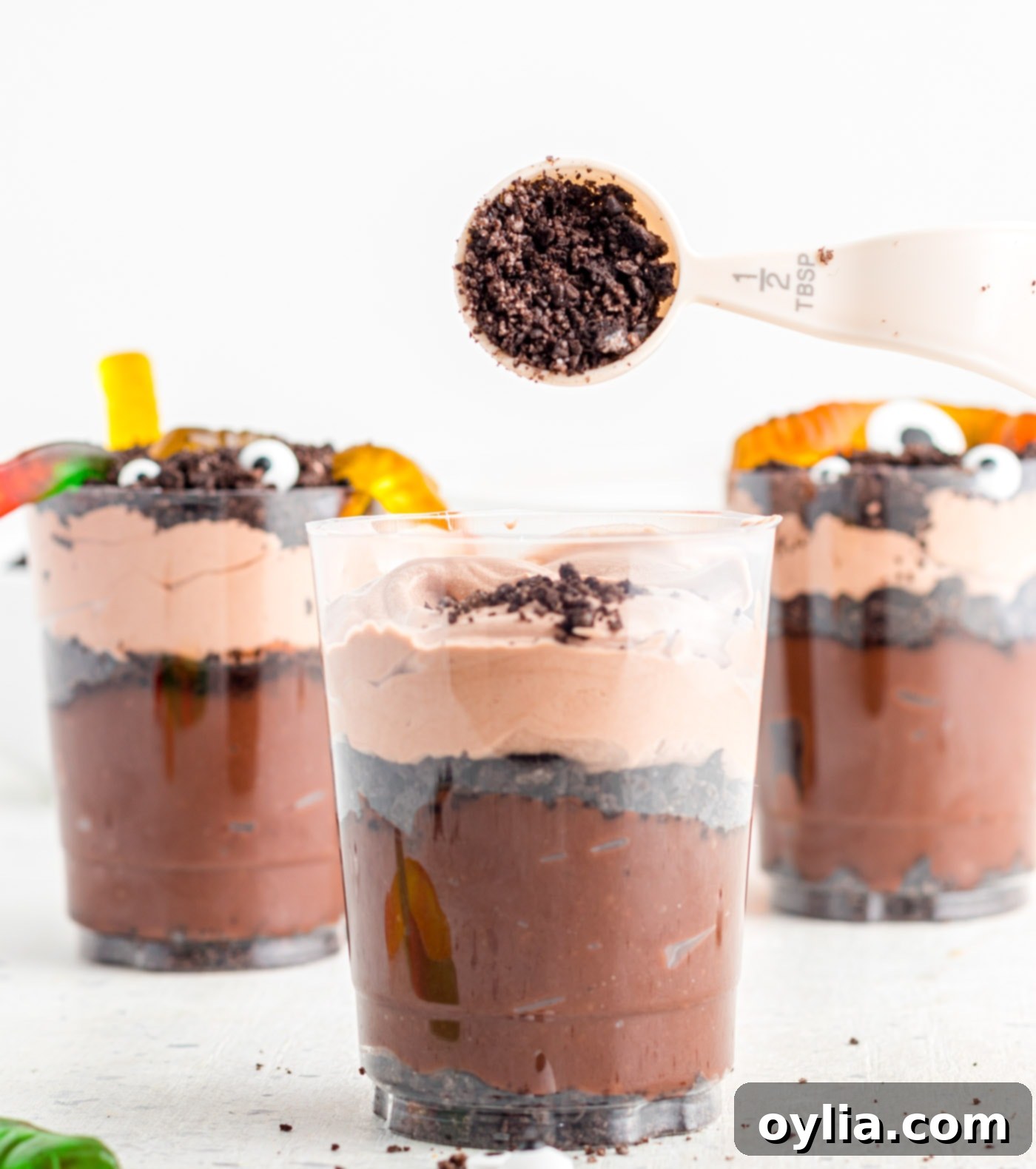 Adding a final layer of crushed Oreo crumbs to the top of Halloween Dirt Cups.