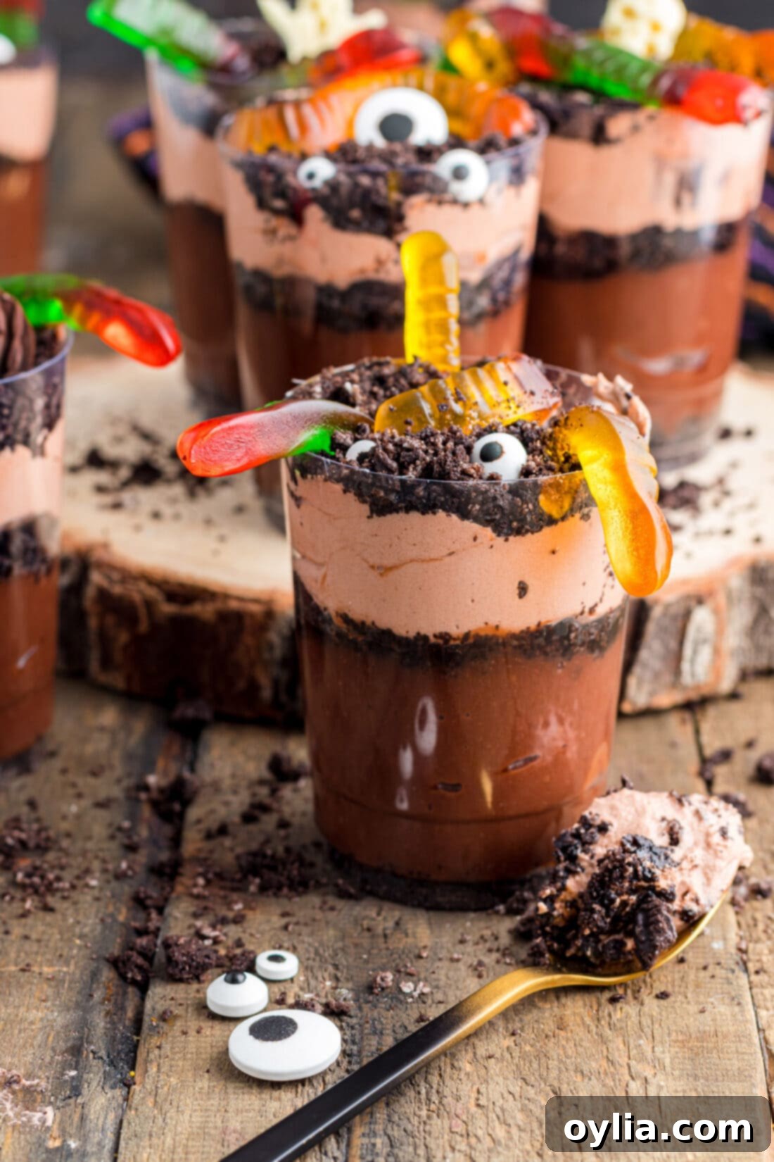 A single Halloween Dirt Cup with several colorful gummy worms emerging from the 'dirt' and a small chocolate pumpkin.