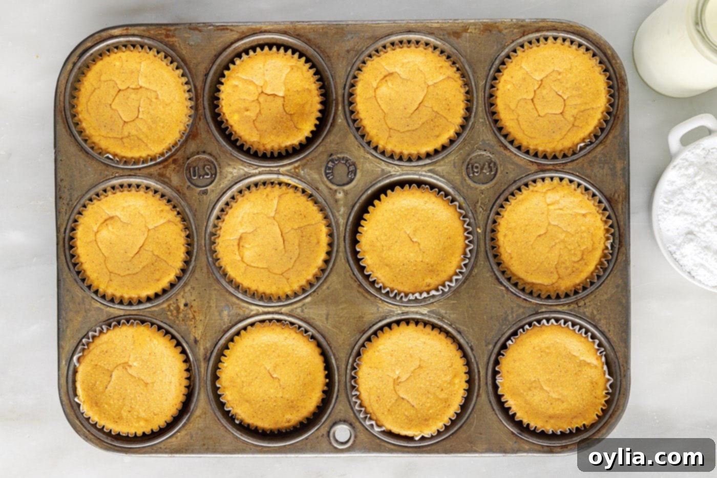 Mini pumpkin cheesecakes baking in a muffin tin, tops appearing matte.