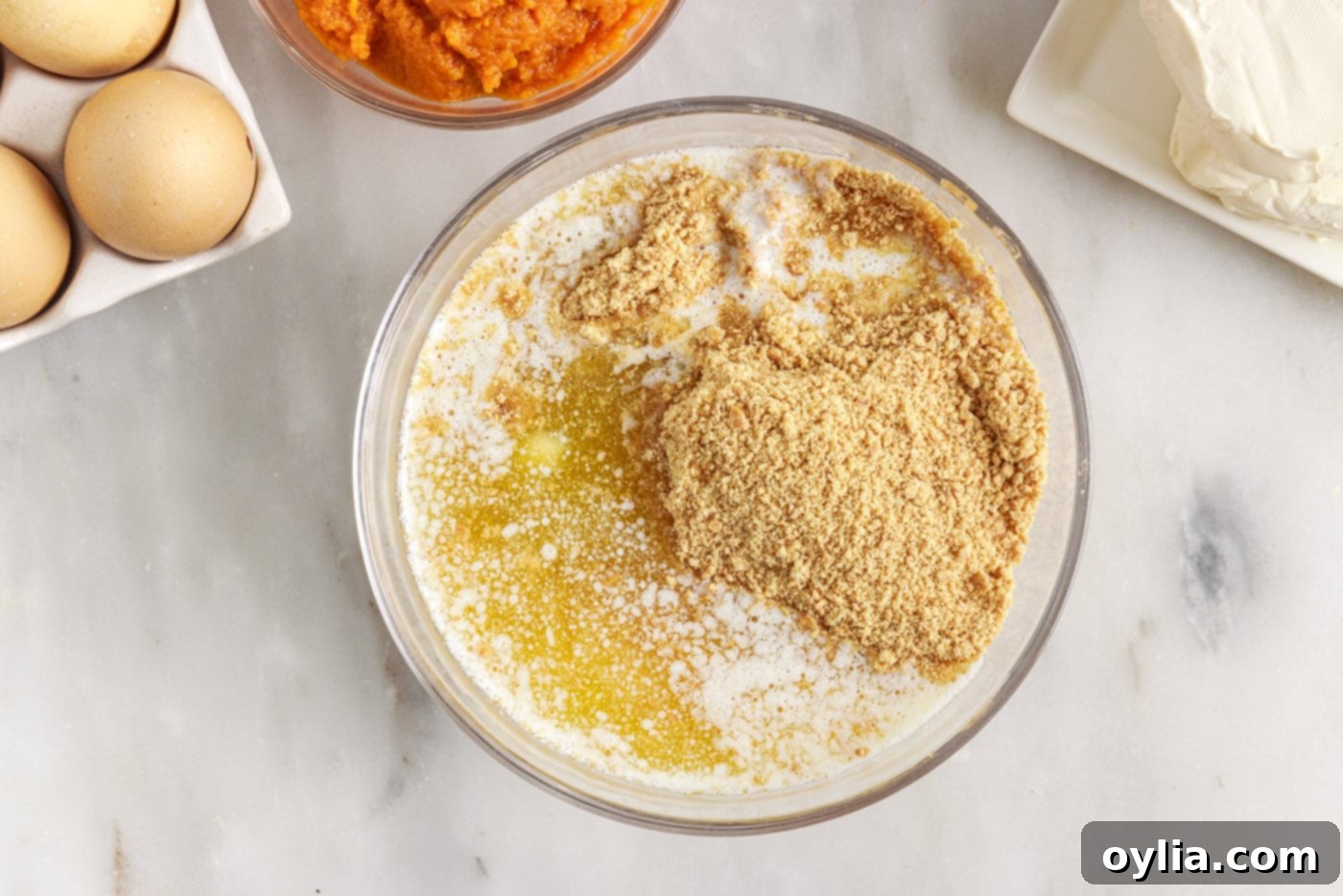 A bowl containing graham cracker crumbs, melted butter, and sugar, ready to be mixed for the cheesecake crust.