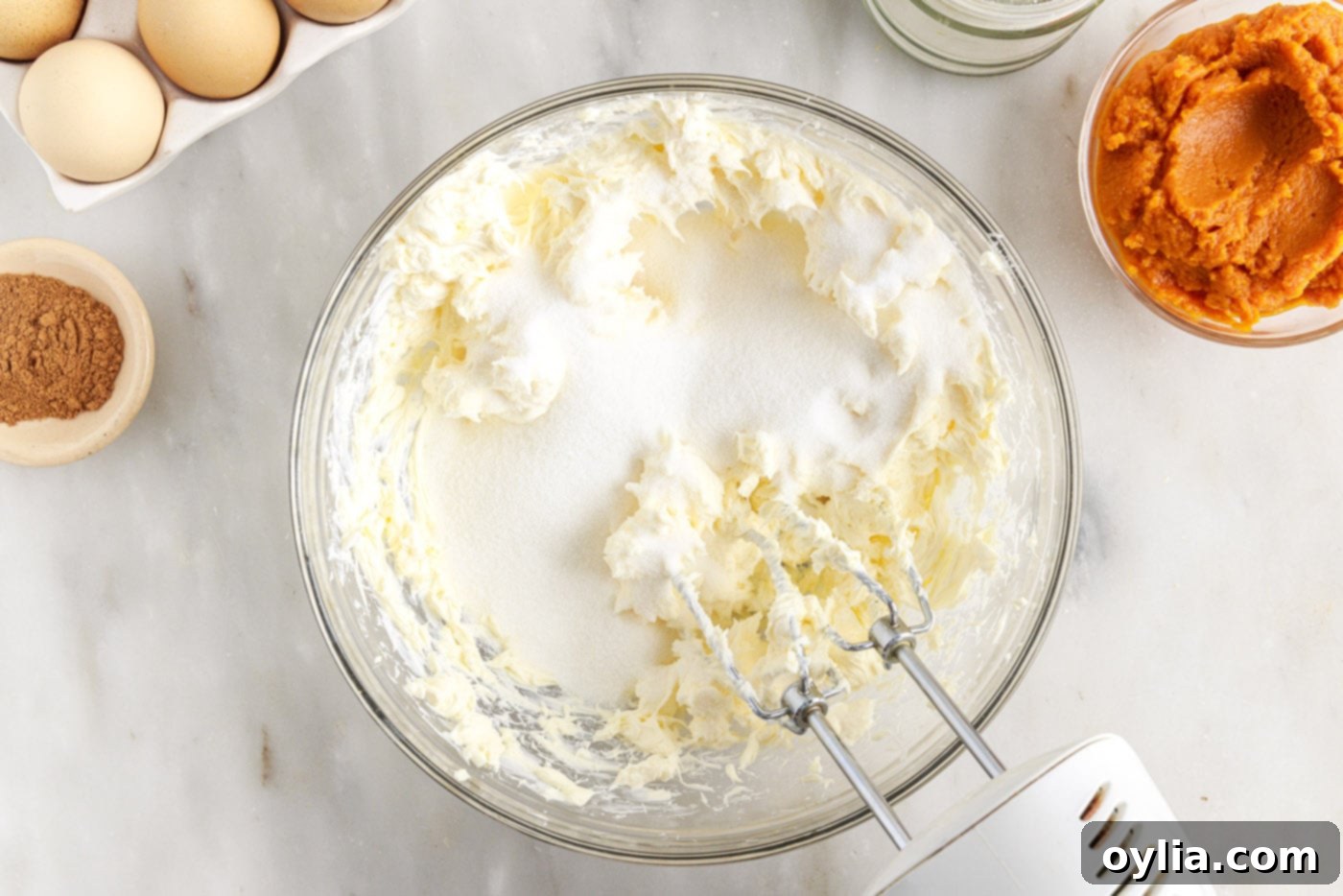 Cream cheese and sugar being beaten together in a large bowl with an electric mixer until smooth.