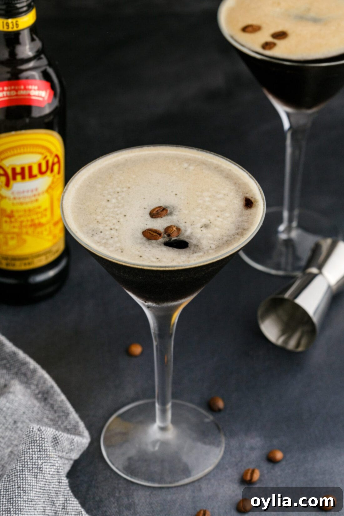 Velvet Buzz 3 Espresso Martini served in a classic martini glass, with a bottle of Kahlua coffee liqueur subtly blurred in the background, suggesting key ingredients.