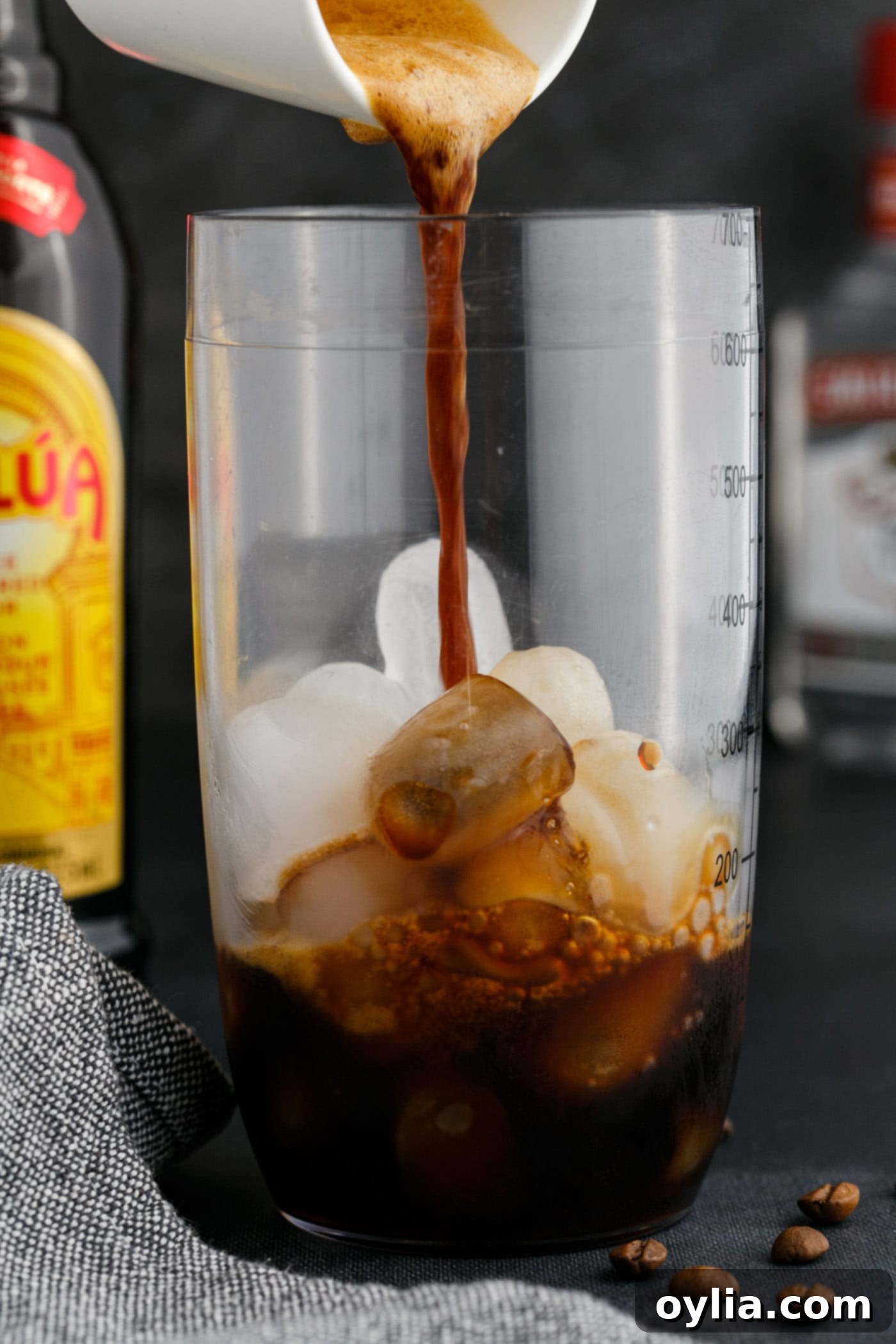Pouring freshly brewed, chilled espresso into a cocktail shaker filled with ice, preparing to mix the Espresso Martini.