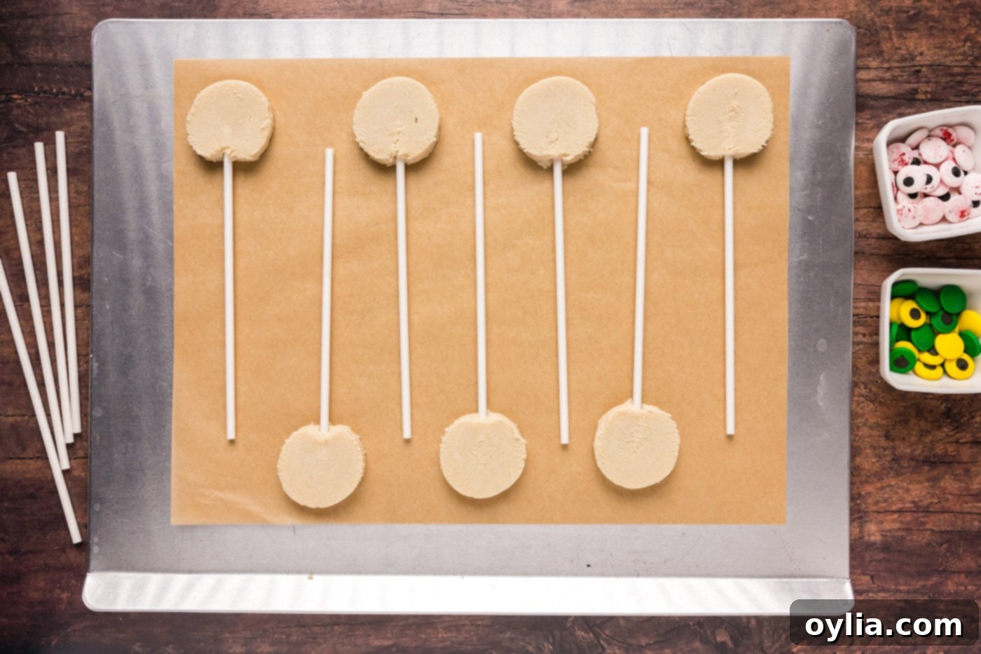 Cookie dough slices with lollipop sticks inserted, on a baking sheet