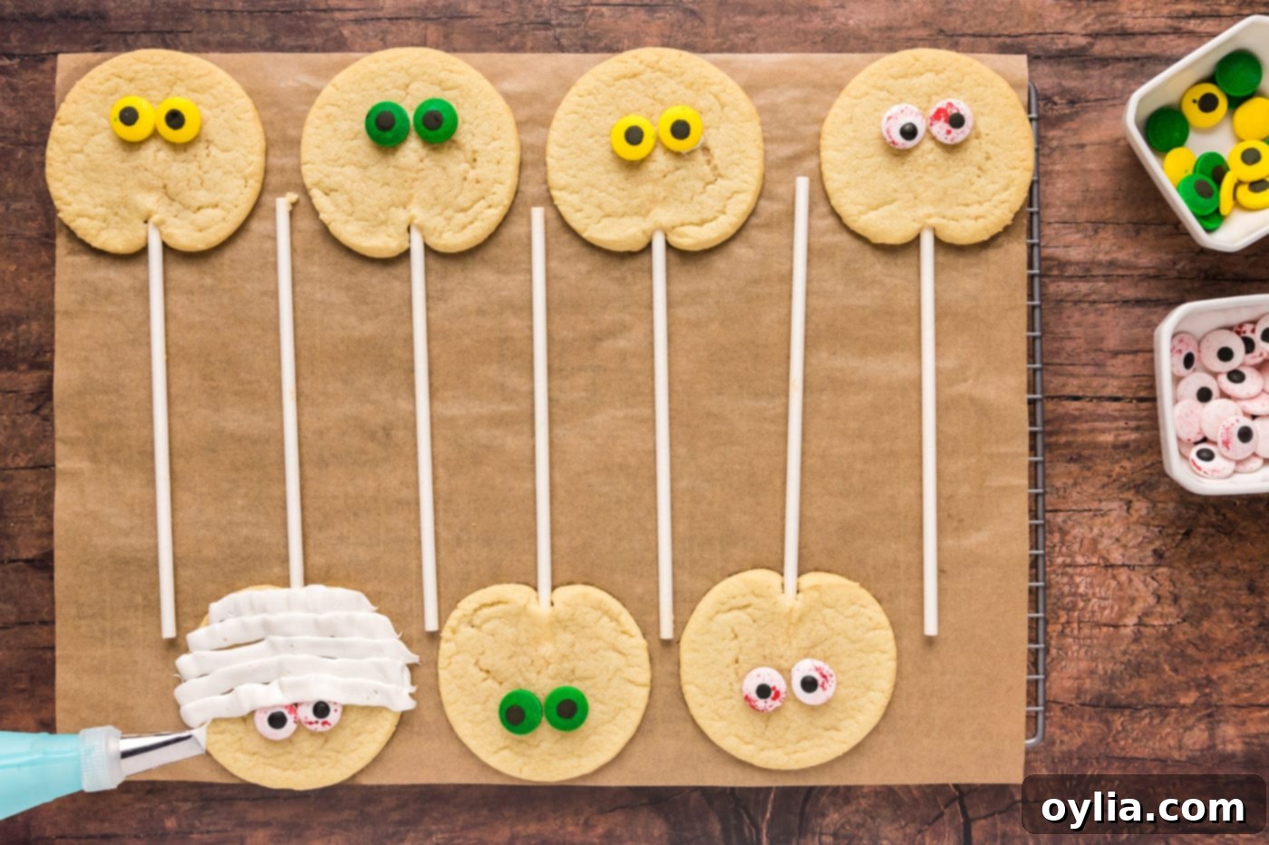 Piping white frosting bandages onto mummy cookies with candy eyeballs