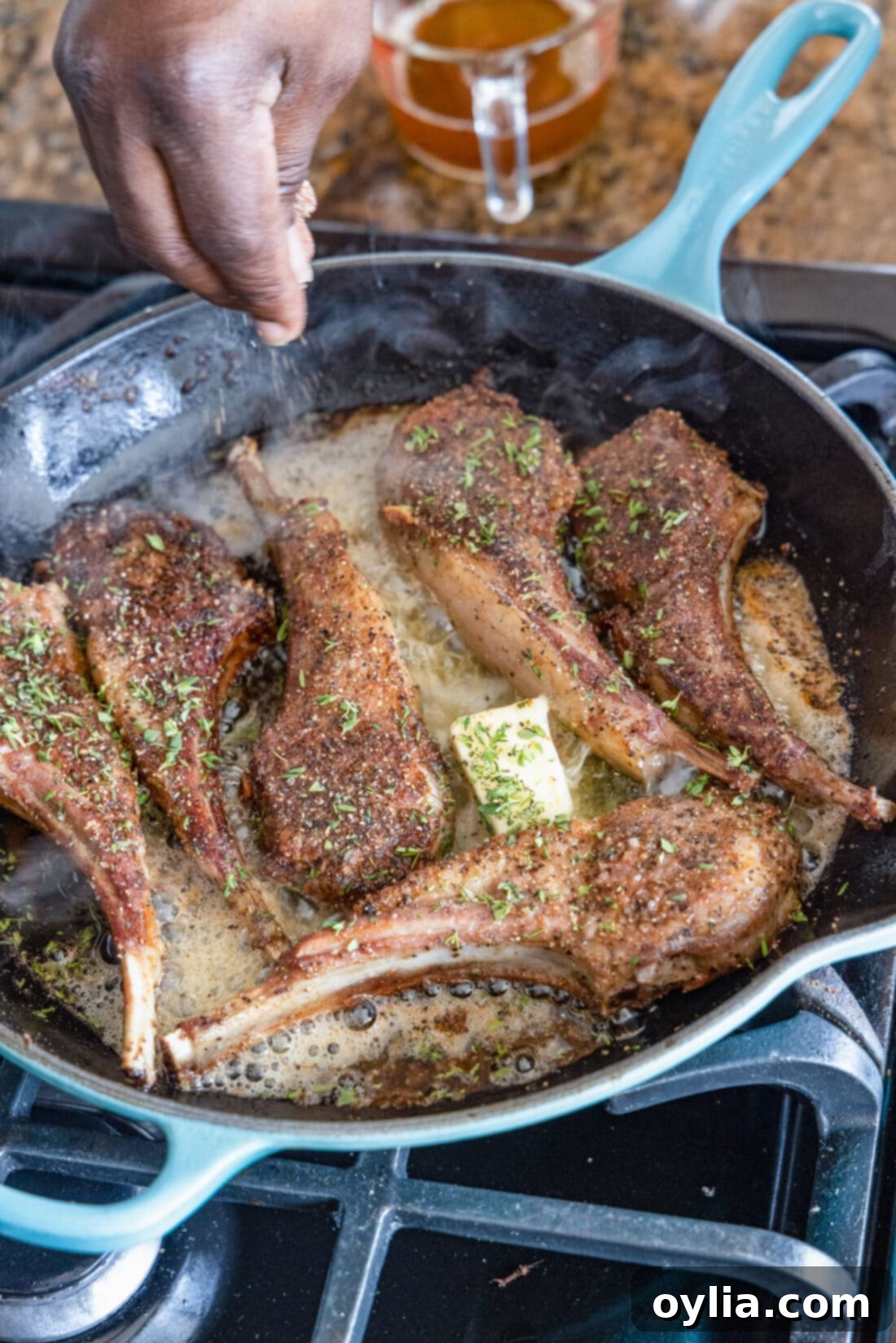 sprinkling thyme of Lollipop Lamb Chops in skillet