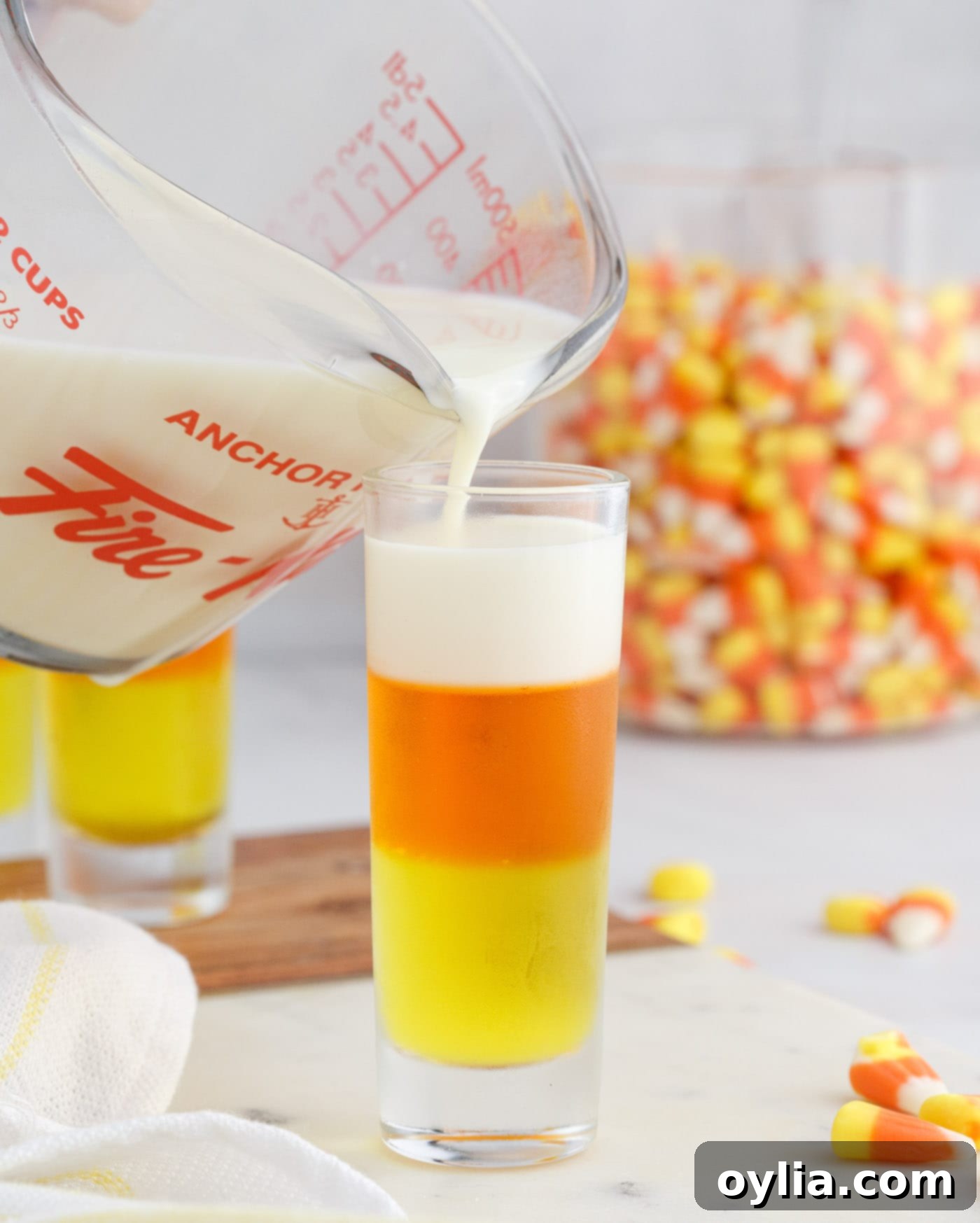 Pouring creamy condensed milk gelatin on top of the orange layer in candy corn jello shots