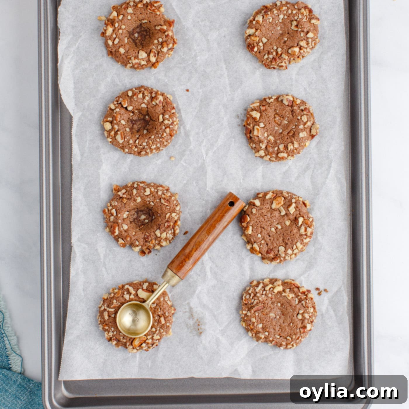 A measuring spoon re-indenting the center of hot, freshly baked thumbprint cookies to create a deeper well for the filling.