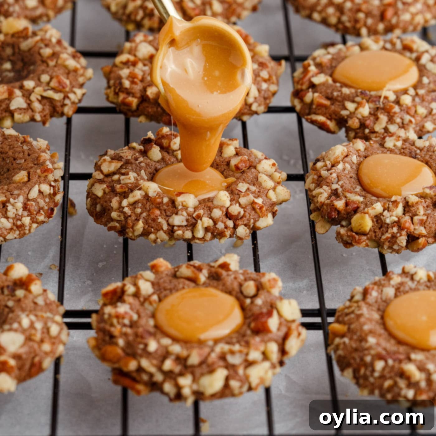 Warm caramel sauce being carefully poured into the indented centers of cooled chocolate thumbprint cookies.