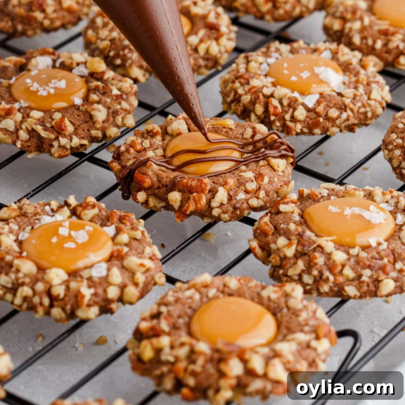 Melted chocolate being artfully drizzled over finished Turtle Thumbprint Cookies, adding a decorative touch.