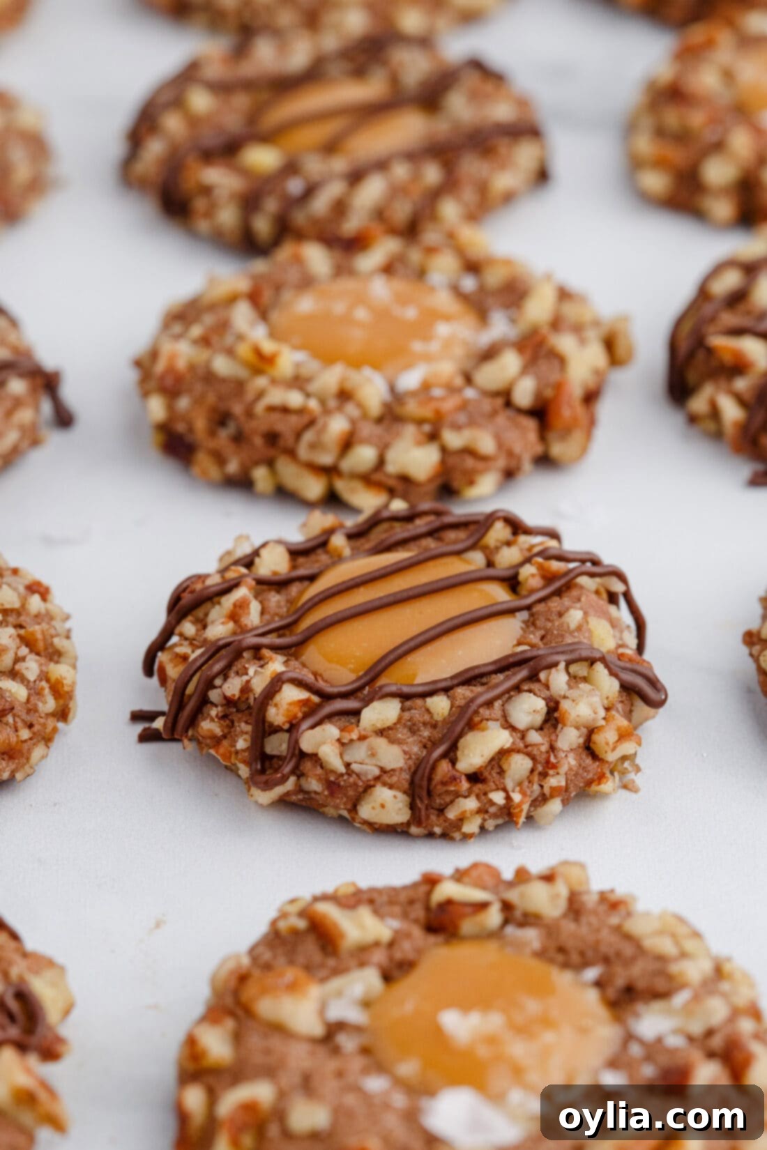 A close-up view of a single Turtle Thumbprint Cookie, highlighting the rich chocolate cookie, the shiny caramel filling, and the textured pecan crust.