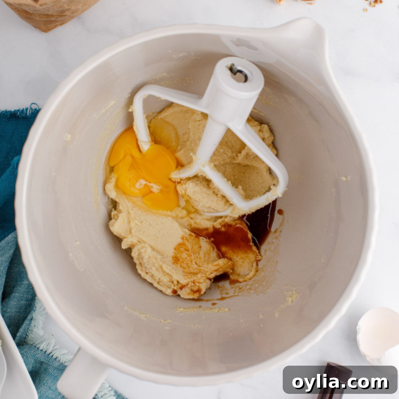 An egg and vanilla extract being added to the creamed butter and sugar mixture in a stand mixer bowl, ready for combining.