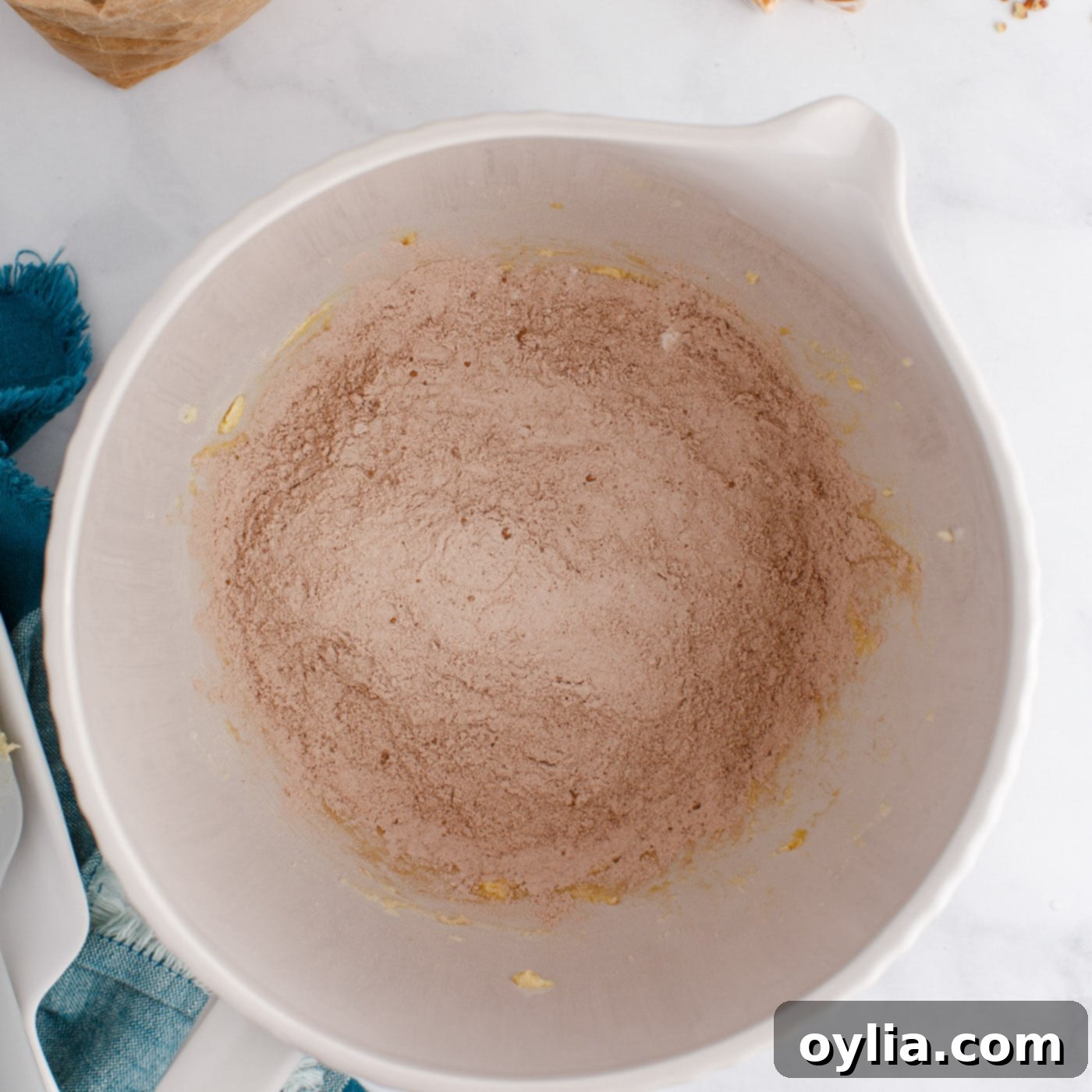 Dry ingredients including flour and cocoa powder being added to the wet mixture in a stand mixer, starting to form a dough.