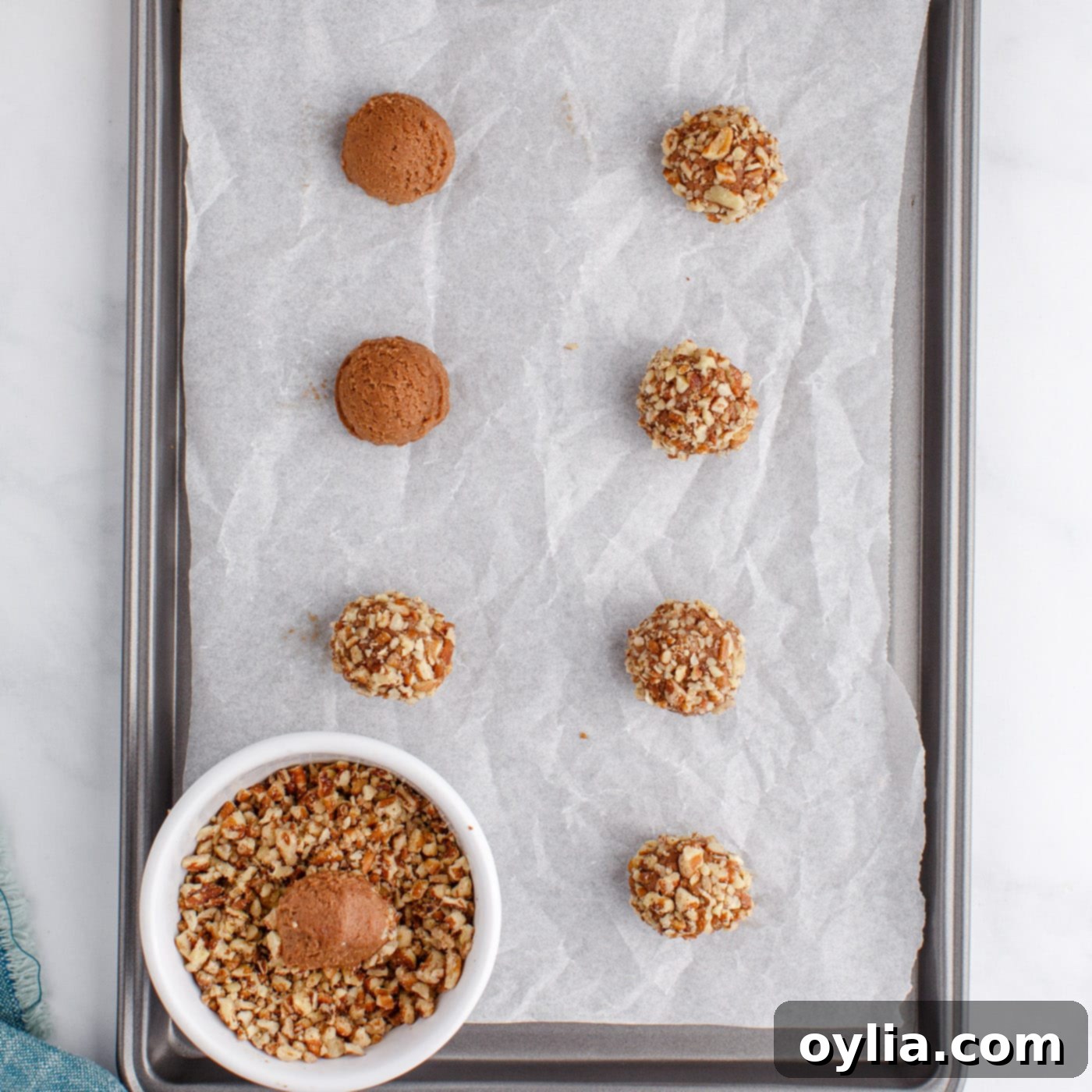 Cookie dough balls being rolled in finely chopped pecans, ready for baking.