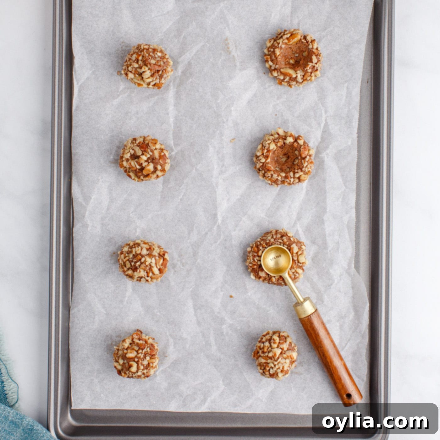 A measuring spoon pressing into the center of unbaked turtle thumbprint cookies to create the indentation.