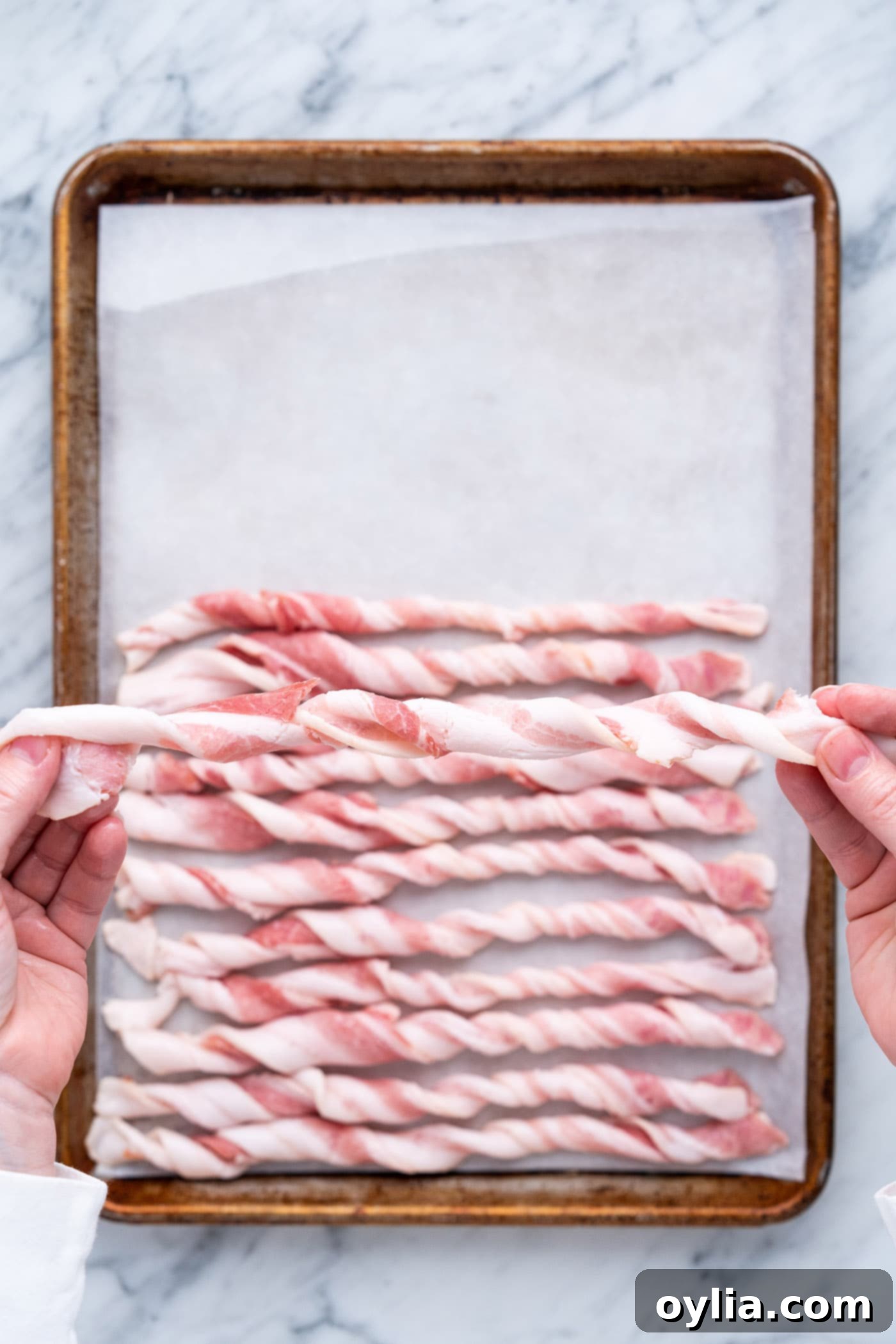Twisted bacon arranged neatly on a parchment-lined baking tray before seasoning.