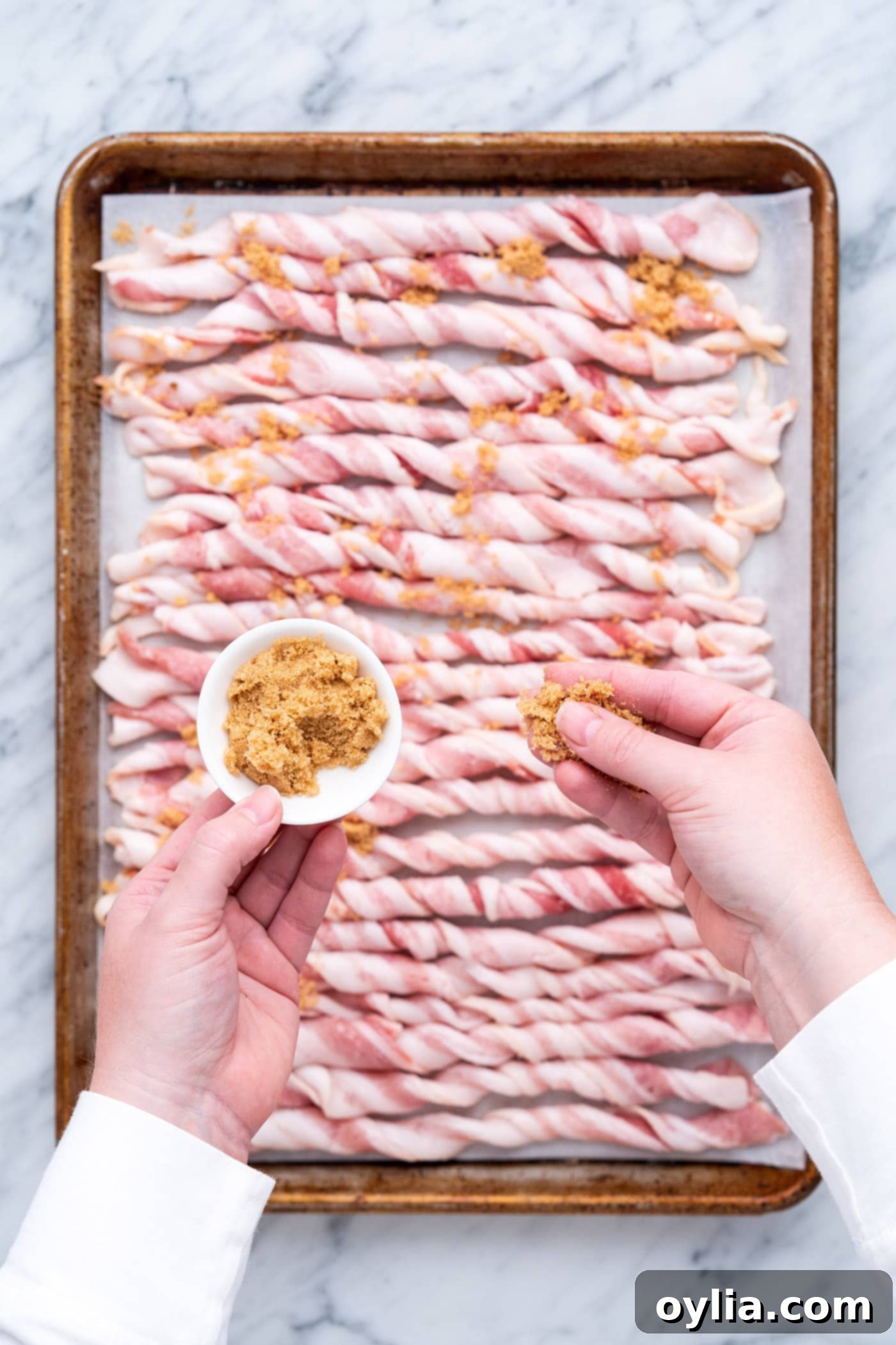 Sprinkling brown sugar evenly over tightly twisted raw bacon strips.